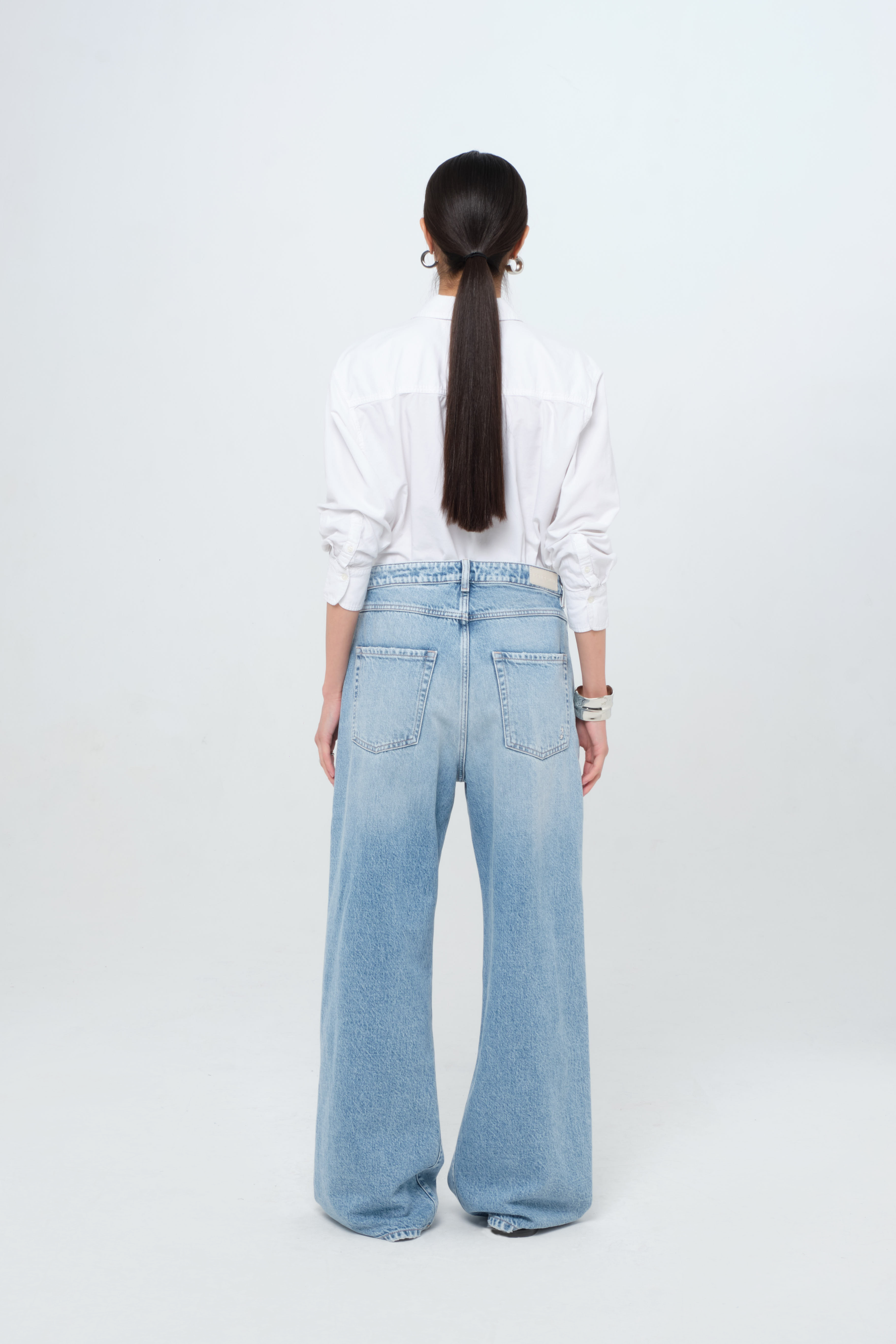 Back view of Debby women’s wide leg jeans in light wash, 100% rigid cotton denim, worn by a model with a white shirt.