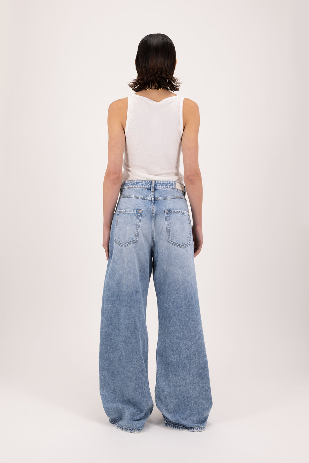 Back view of Debby women’s wide leg jeans in river wash, 100% rigid cotton denim, worn by a model with a white tank top.