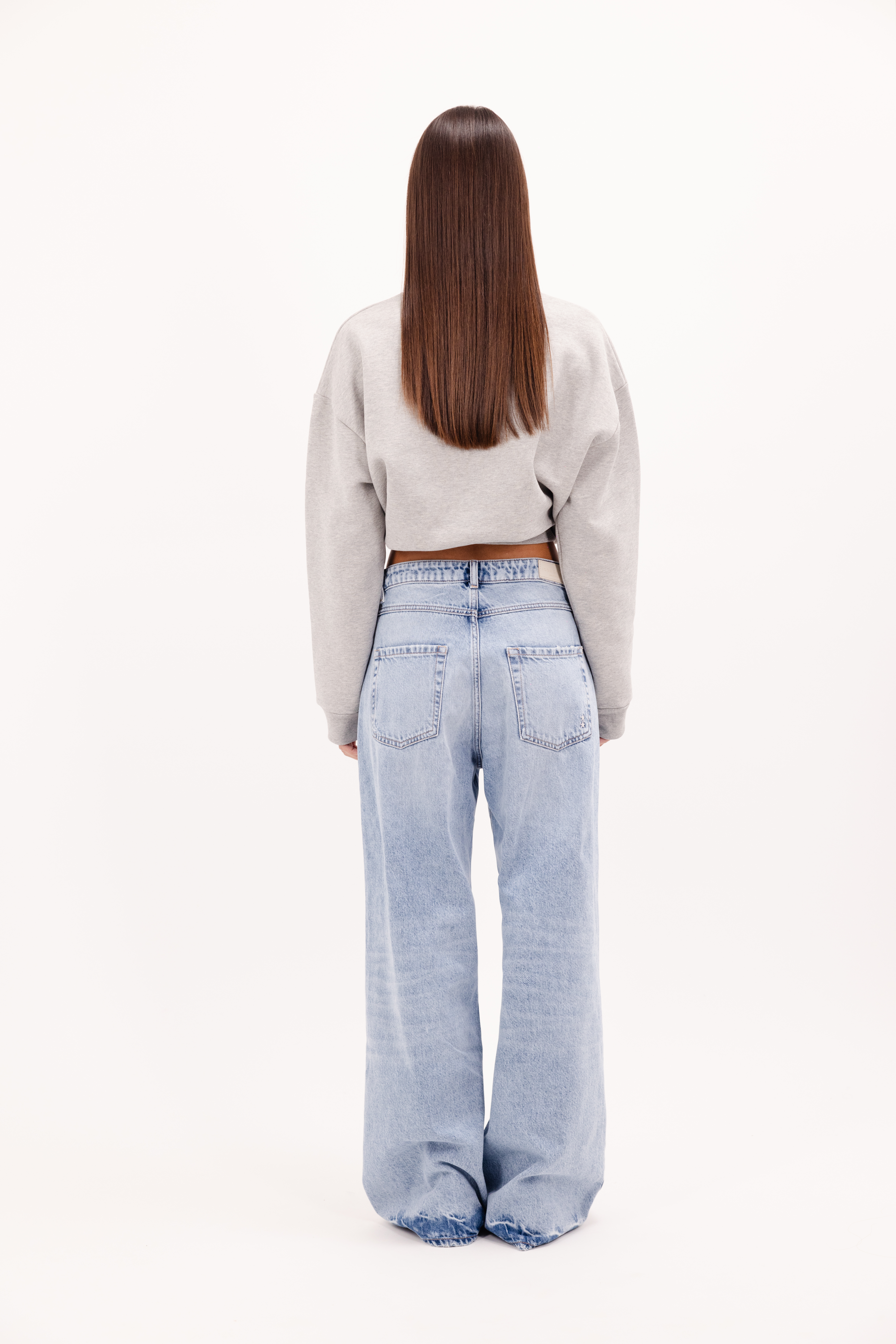 Back view of Debby women’s wide leg jeans in sky blue wash, 100% rigid cotton denim, worn by a model with a gray sweatshirt.