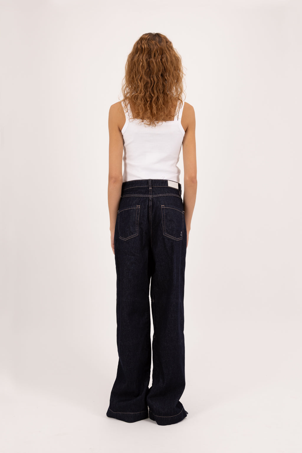 Back view of Faby women’s wide leg jeans in indigo raw, 100% rigid cotton denim, worn by a model with a white tank top.