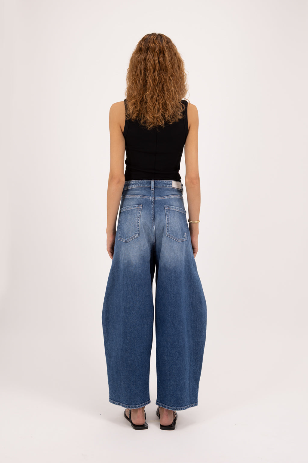 Back view of Ginny women’s balloon jeans in eclipse wash, 100% rigid cotton denim, worn by a model with a black tank top.
