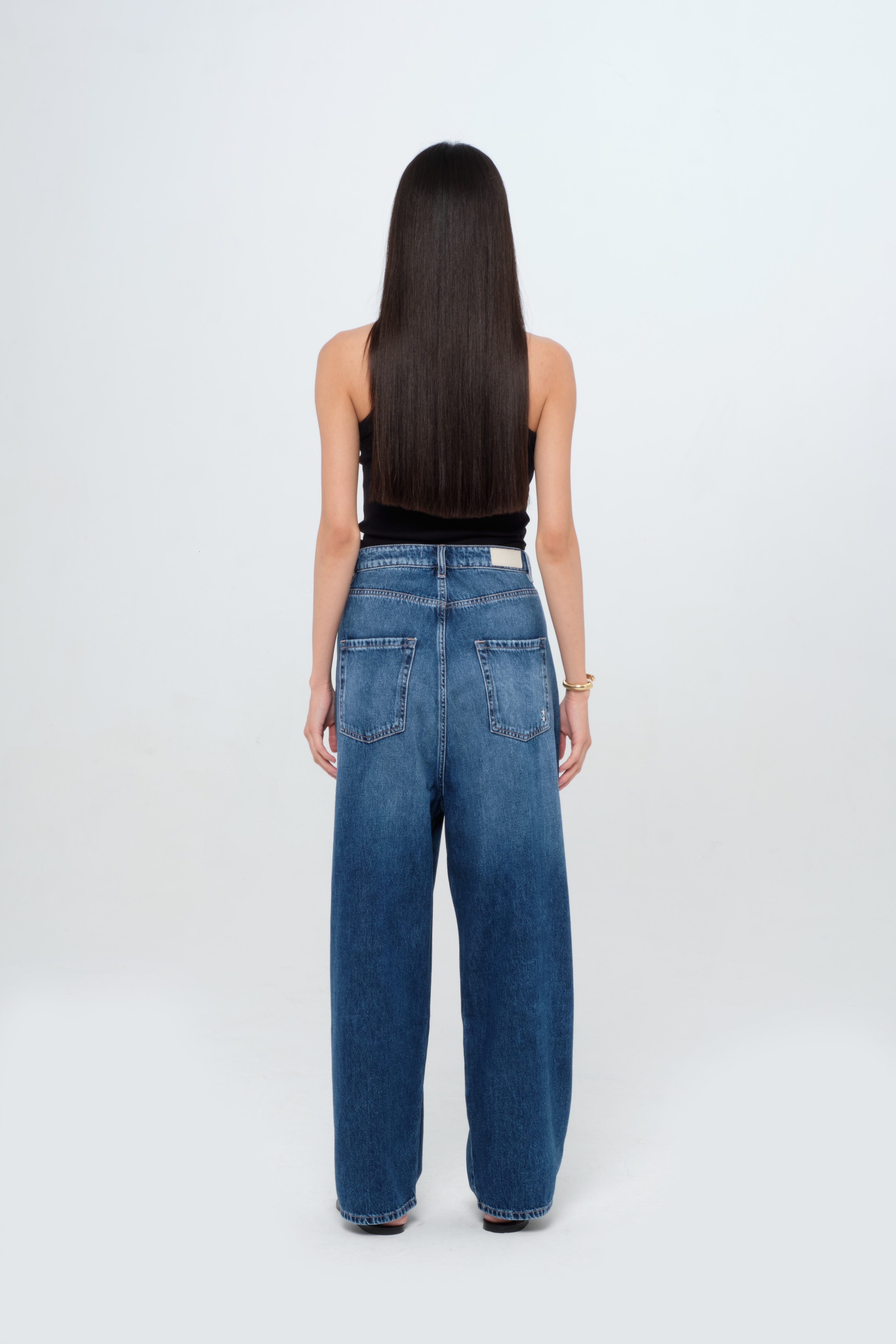 Back view of Holly women’s wide leg jeans in medium wash, 100% rigid cotton denim, worn by a model with a black tank top.
