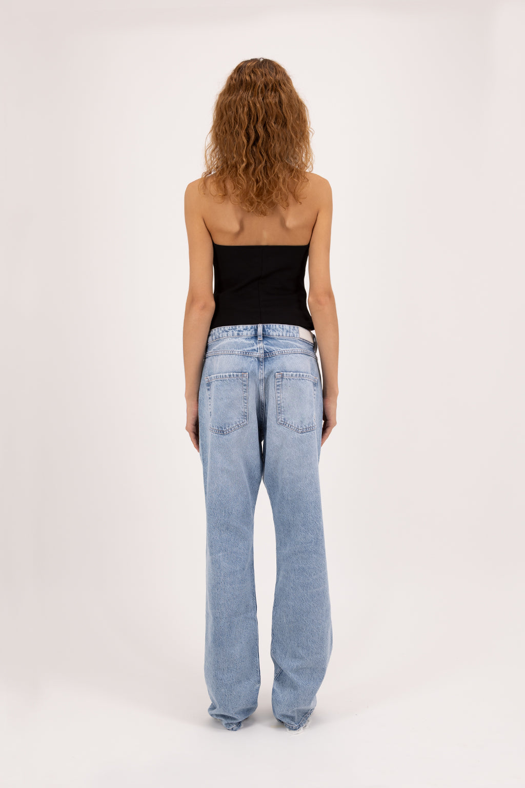 Back view of Iris Eco women’s wide leg jeans in arid blue wash, 100% organic rigid cotton denim, worn by a model with a black top.