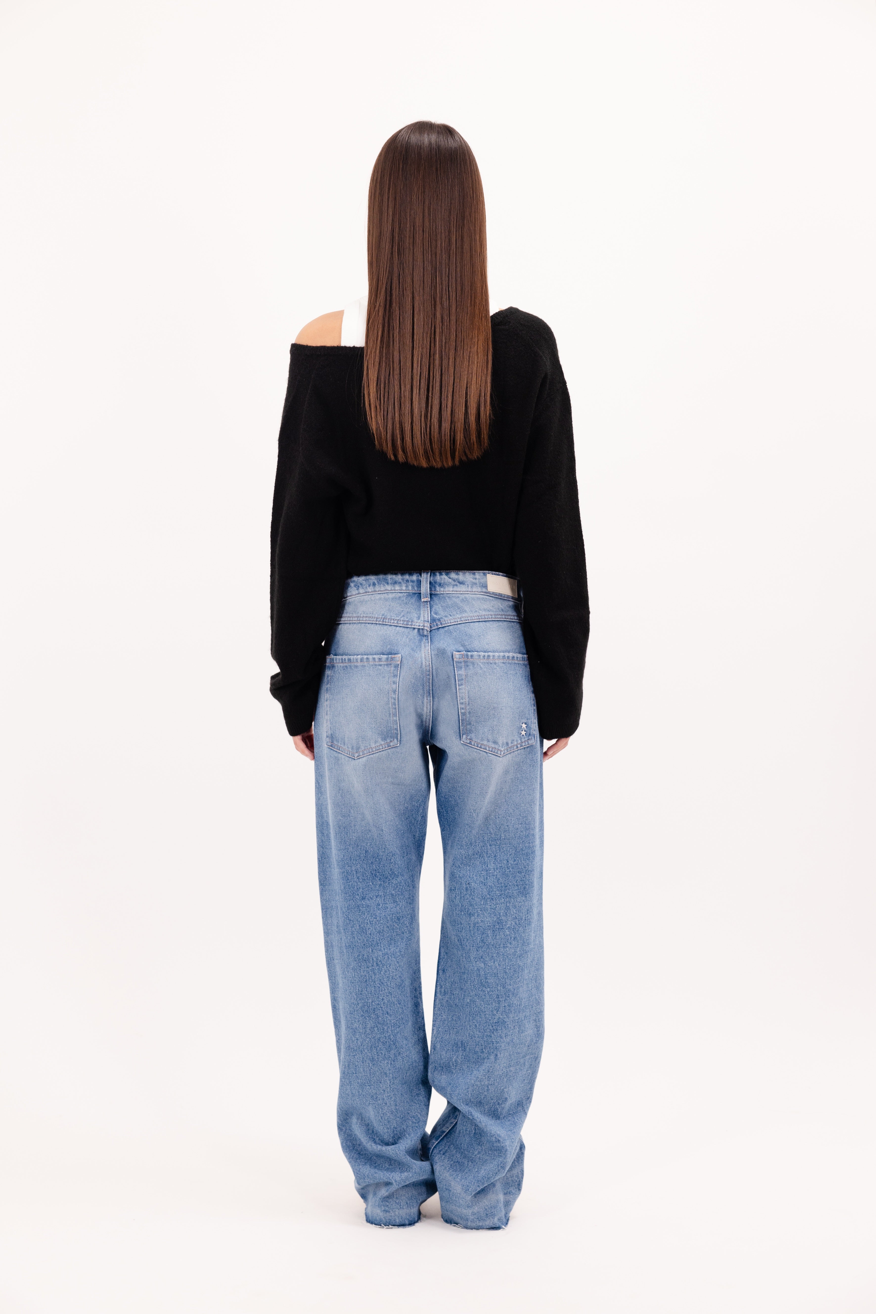 Back view of Iris Eco women’s wide leg jeans in medium wash, 100% rigid organic cotton denim, worn by a model with a black sweater.
