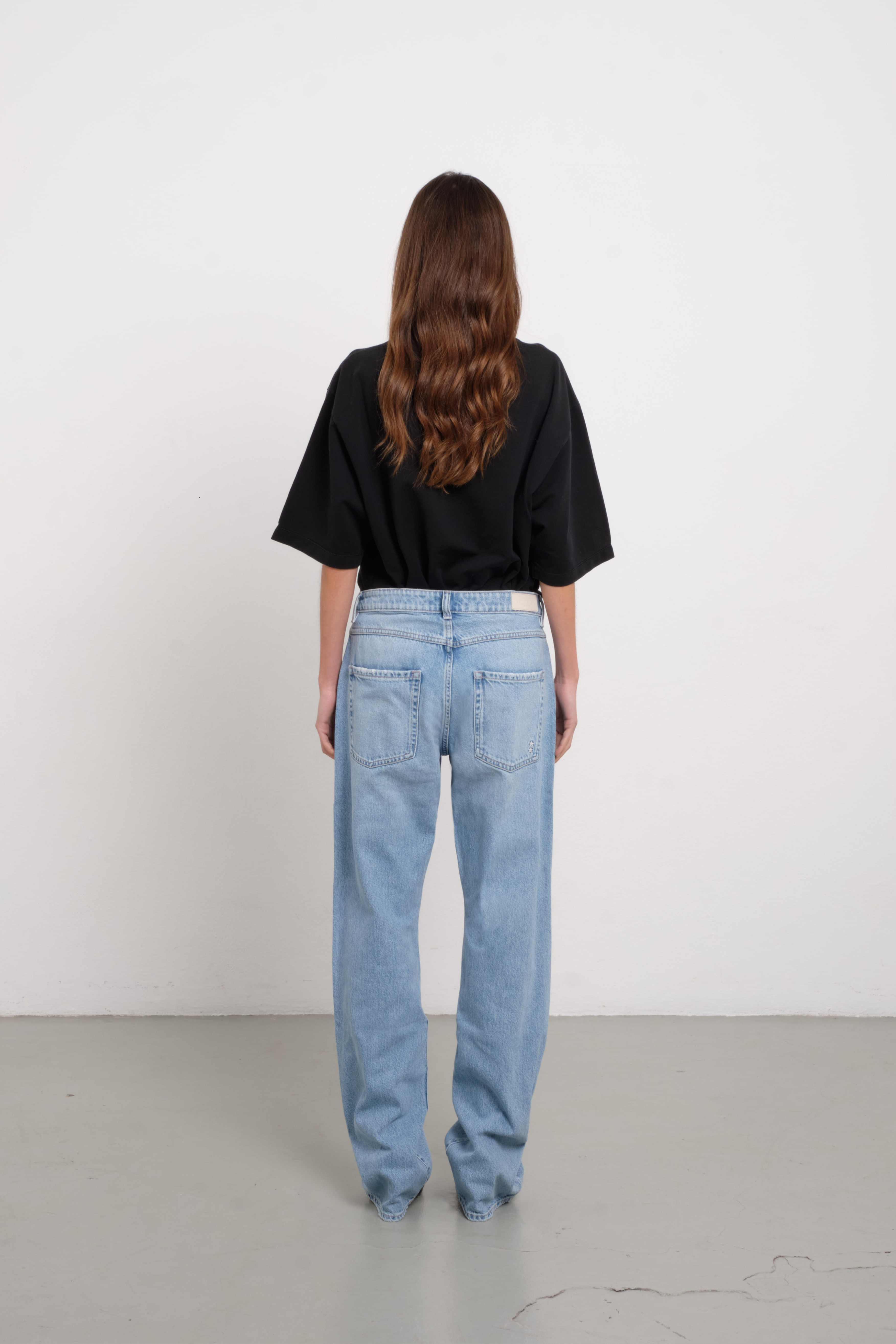 Back view of Iris women’s wide leg jeans in light wash, 100% rigid cotton denim, worn by a model with a black shirt.
