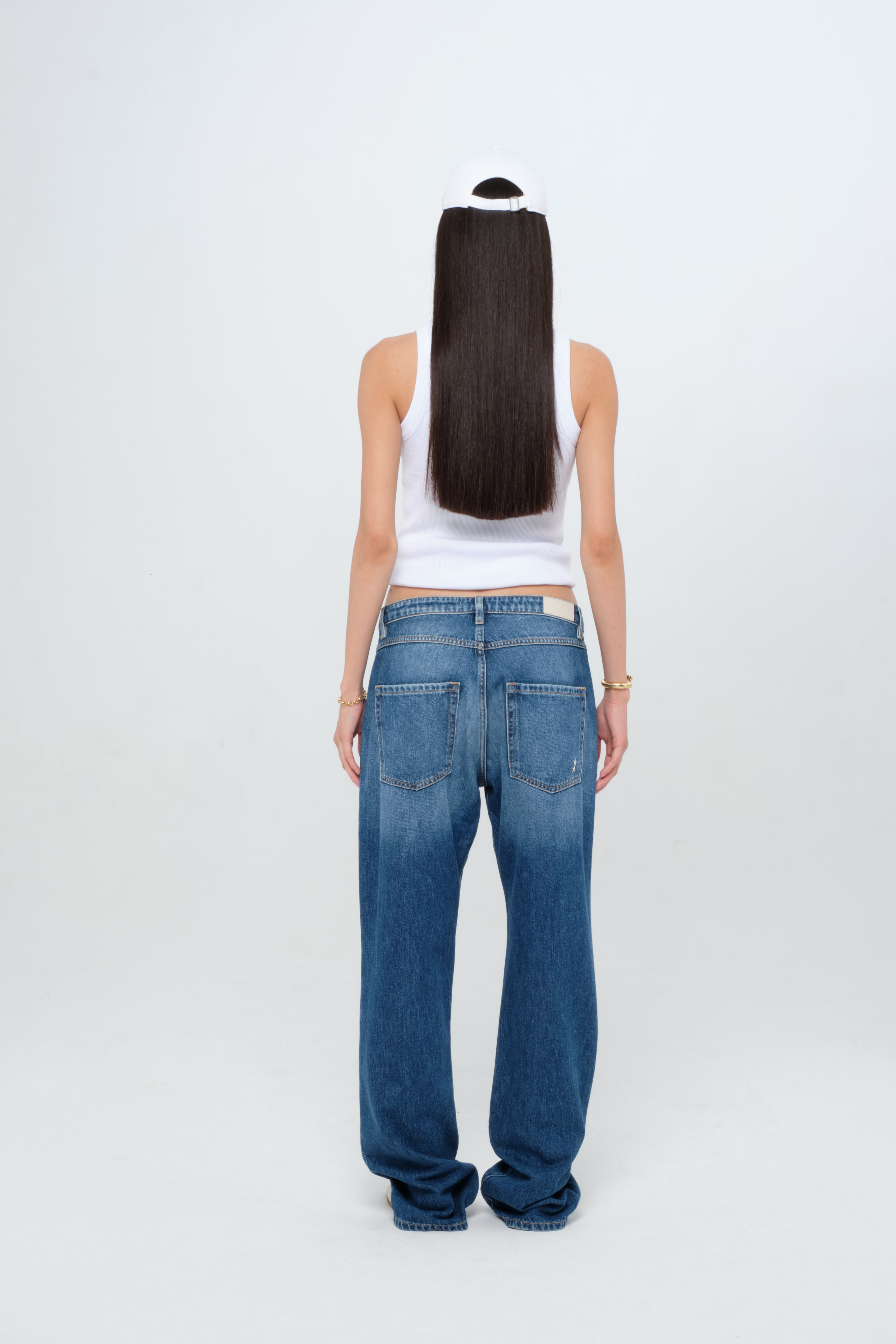 Back view of Iris women’s wide leg jeans in medium wash, 100% rigid cotton denim, worn by a model with a white tank top.
