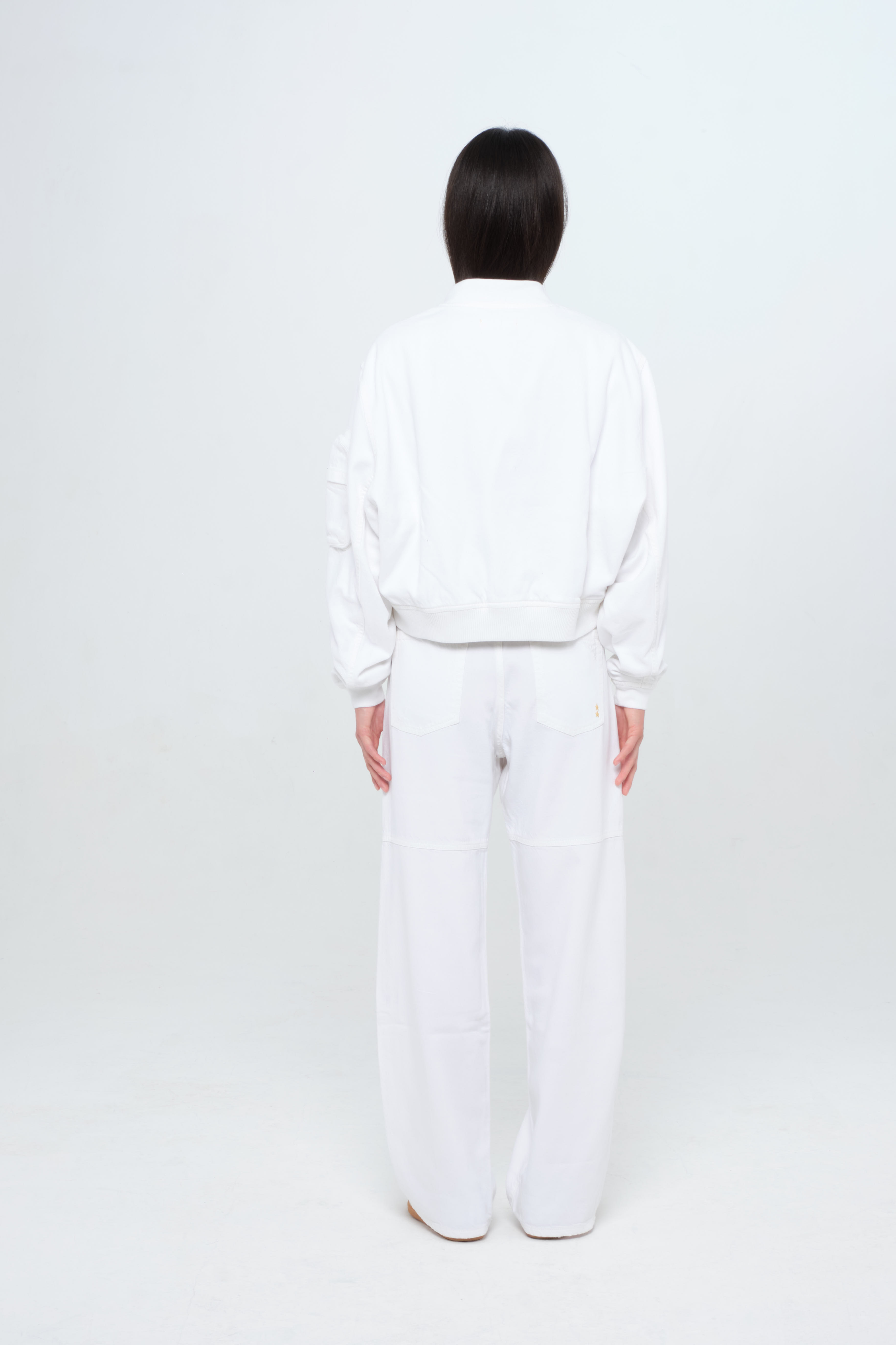 Back view of Ivy women’s jacket in light wash, 100% rigid soft cotton denim, worn by a model with white jeans.
