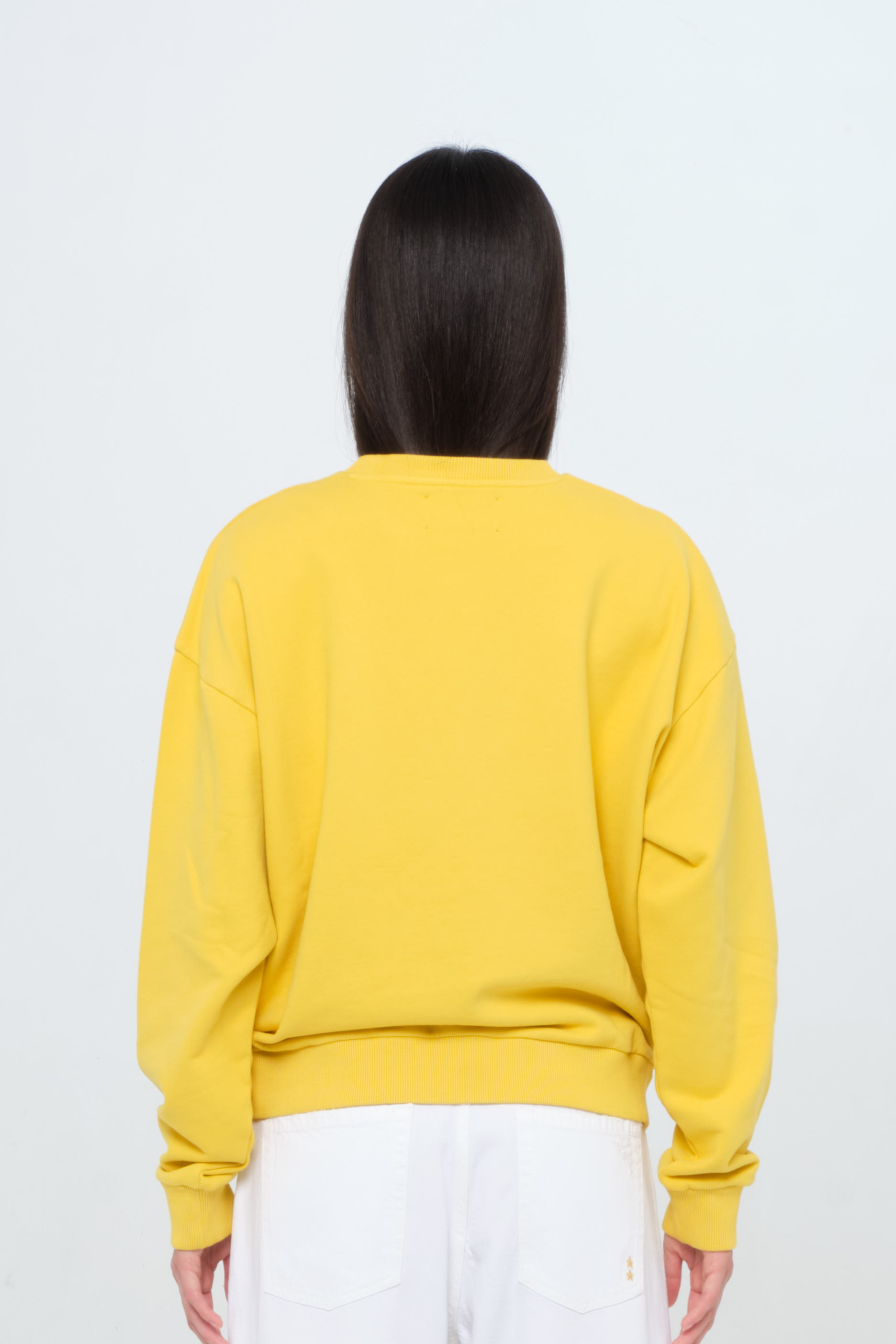 Back view of Jamie women’s sweatshirt in sunny, 100% cotton, worn by a model with white jeans.
