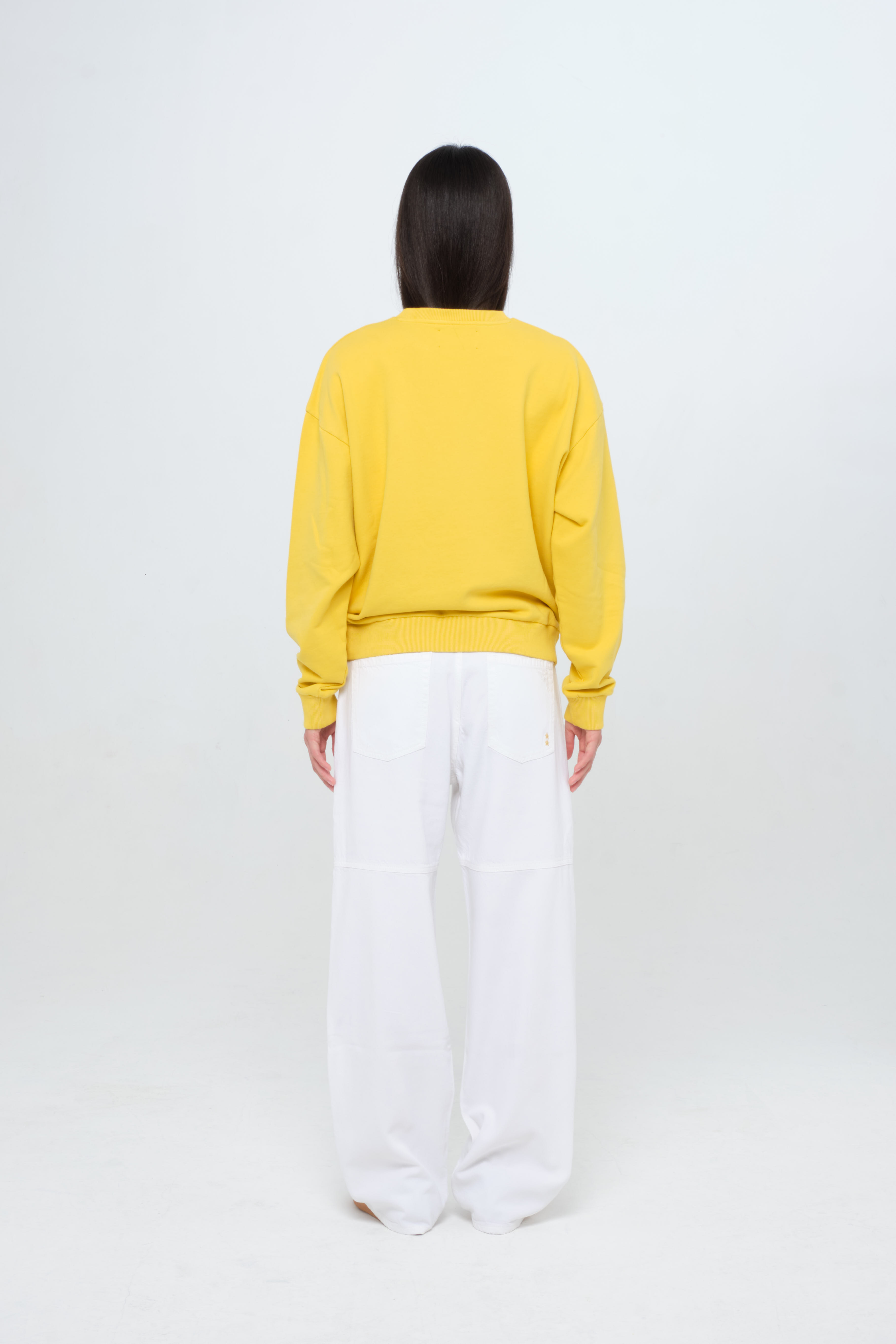 Back view of Jamie women’s sweatshirt in sunny, 100% cotton, worn by a model with white jeans.
