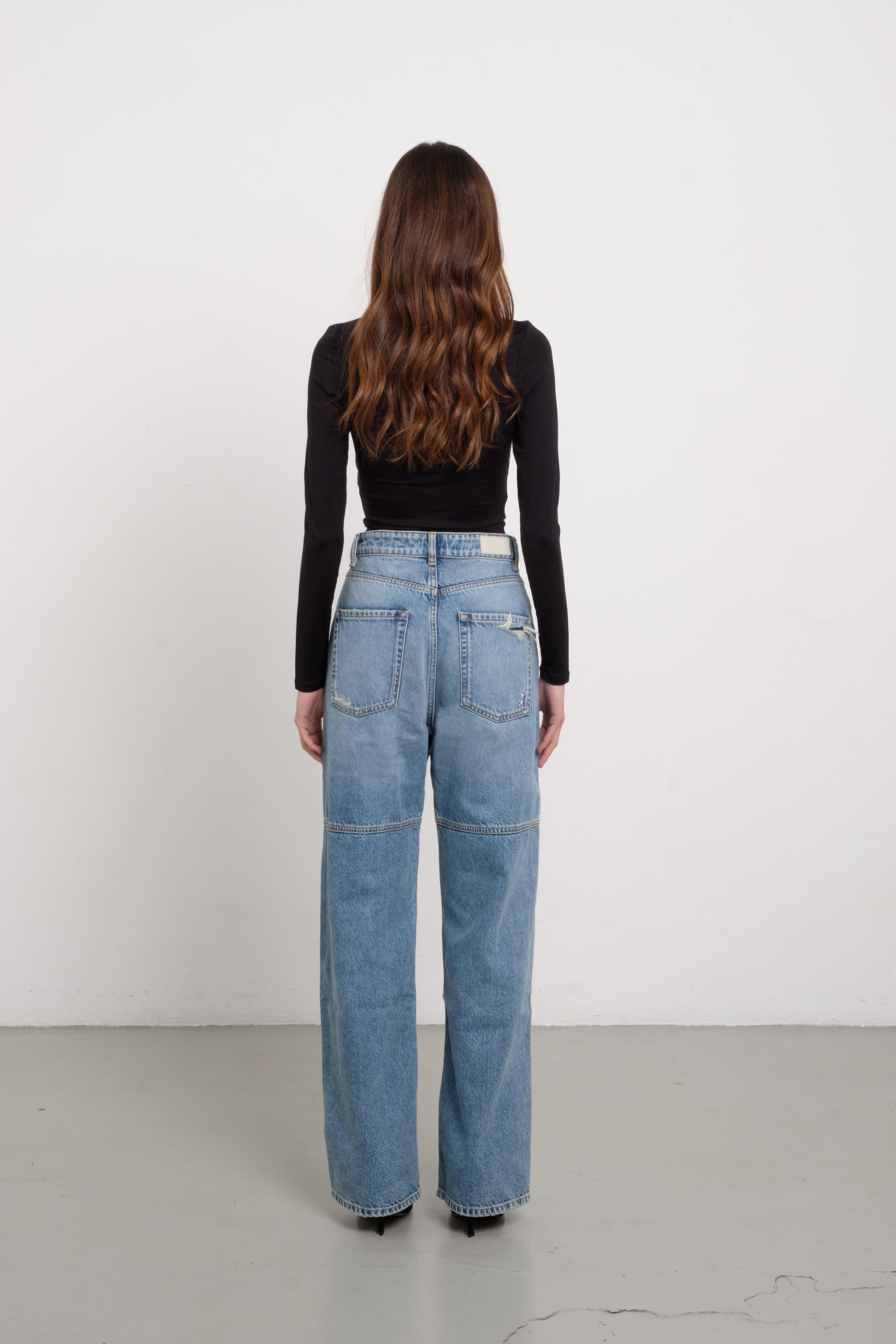 Back view of Jenny women’s straight leg jeans in medium wash, 100% rigid cotton denim, worn by a model with a black top.
