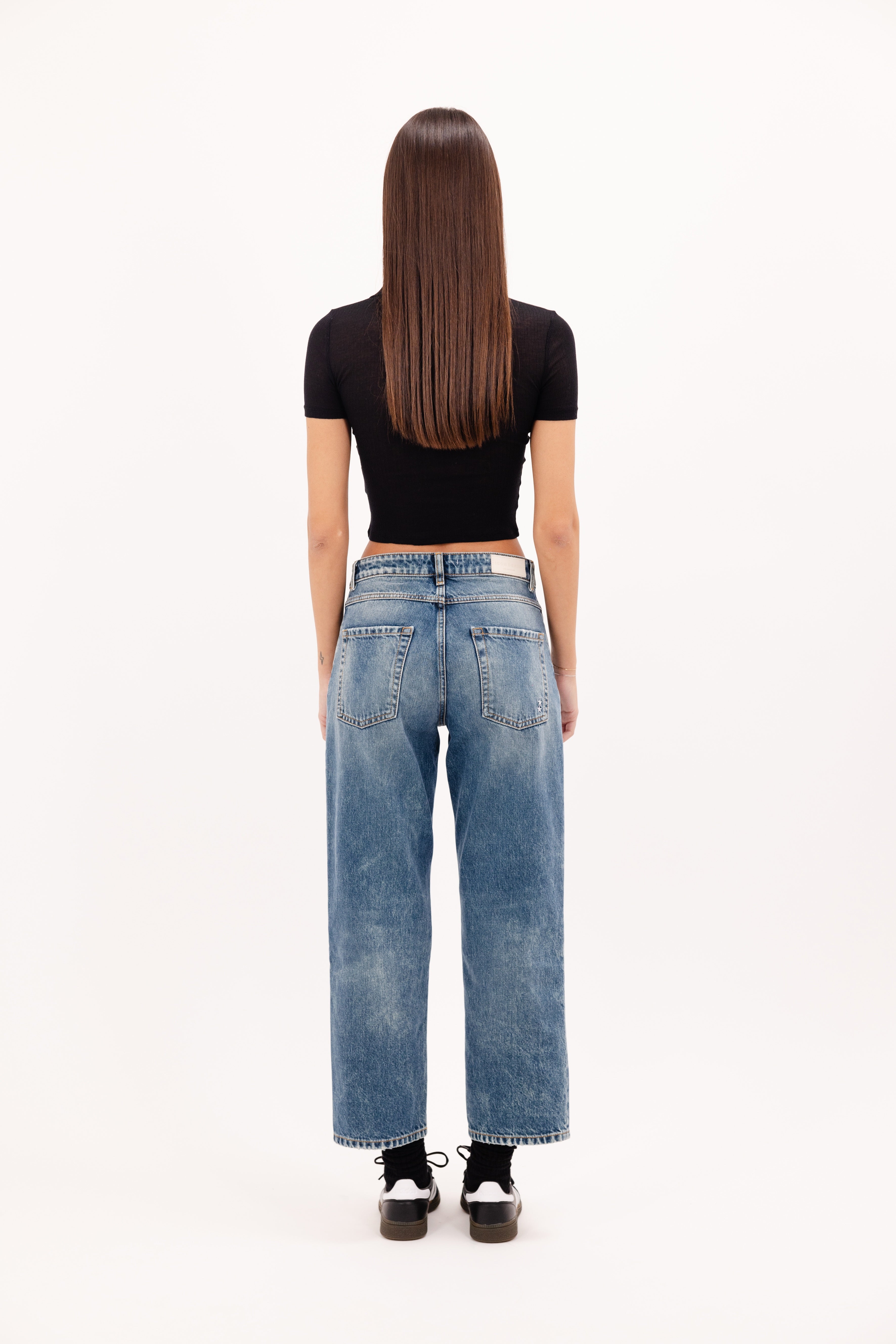 Back view of Jill women’s straight leg jeans in aged stone wash, 100% rigid cotton denim, worn by a model with a black top.