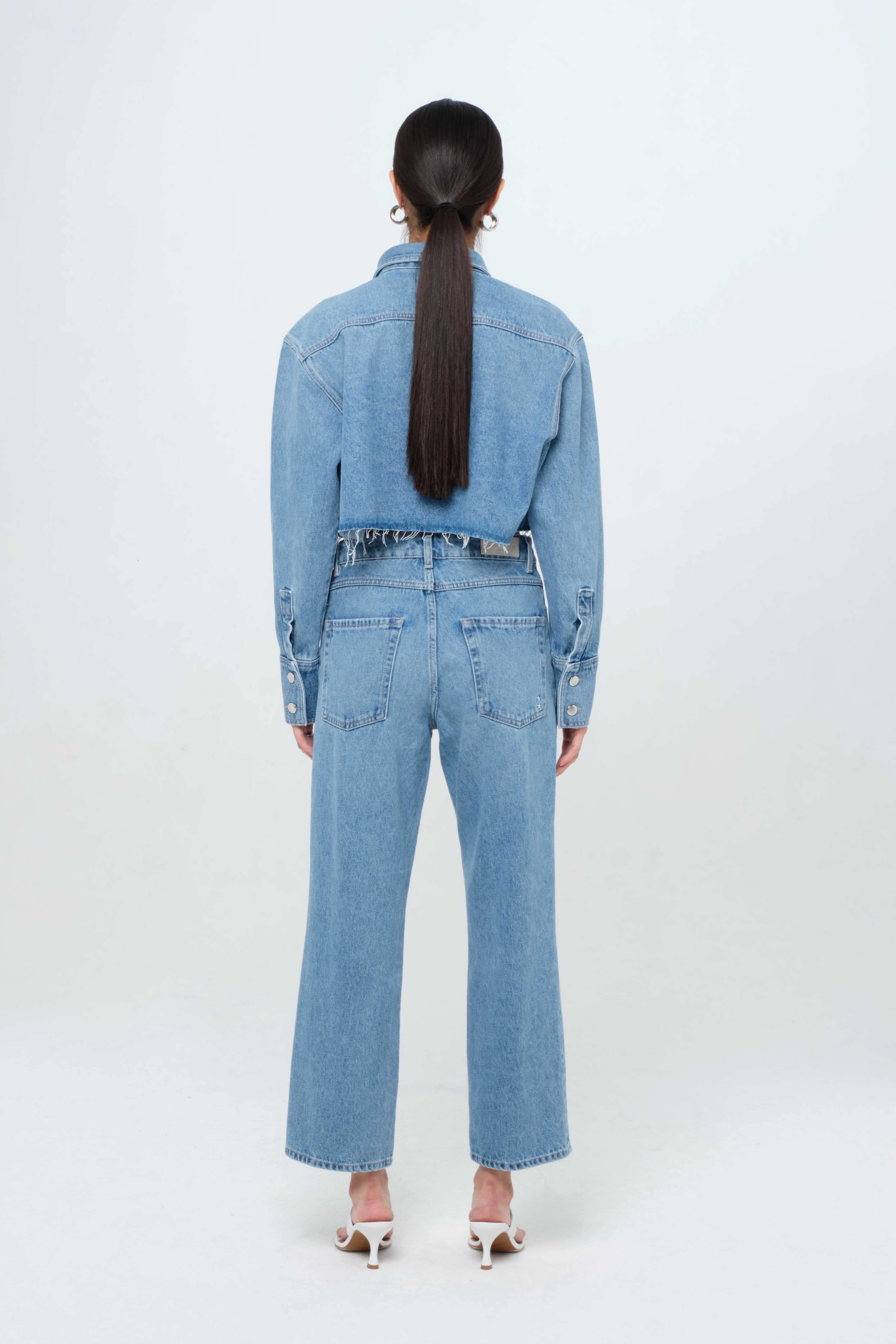 Back view of Jill women’s straight leg jeans in medium wash, 100% rigid organic cotton denim, worn by a model with a crop denim shirt.

