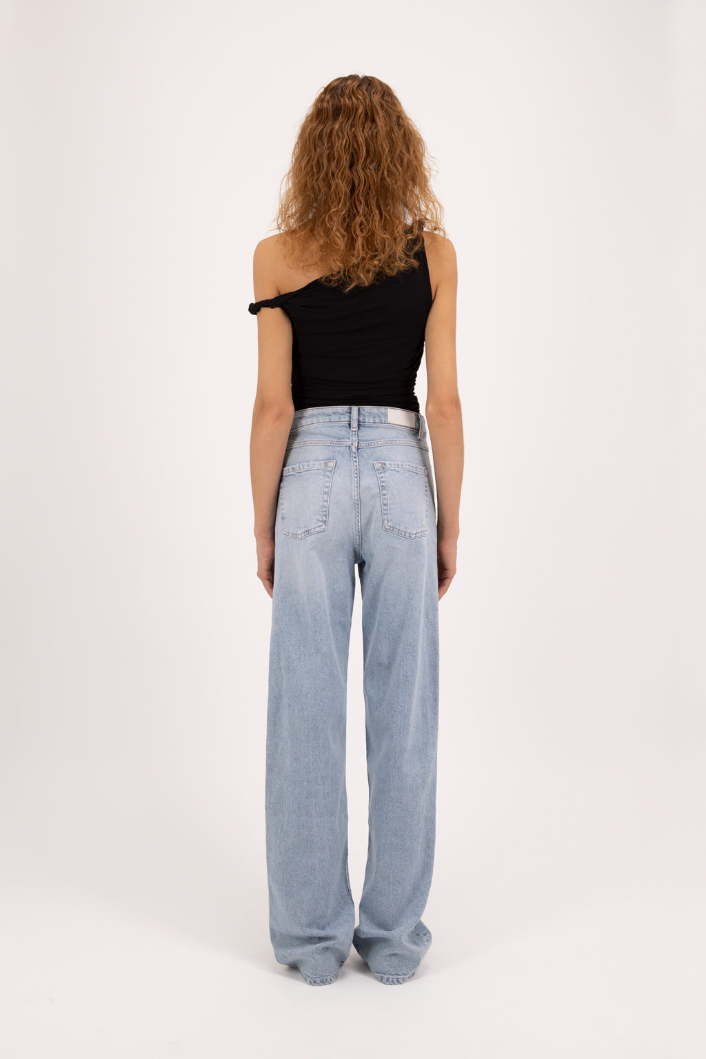 Back view of Joia women’s mom jeans in sky blue wash, 99% cotton denim and 1% Elastan fibers, worn by a model with a black top.