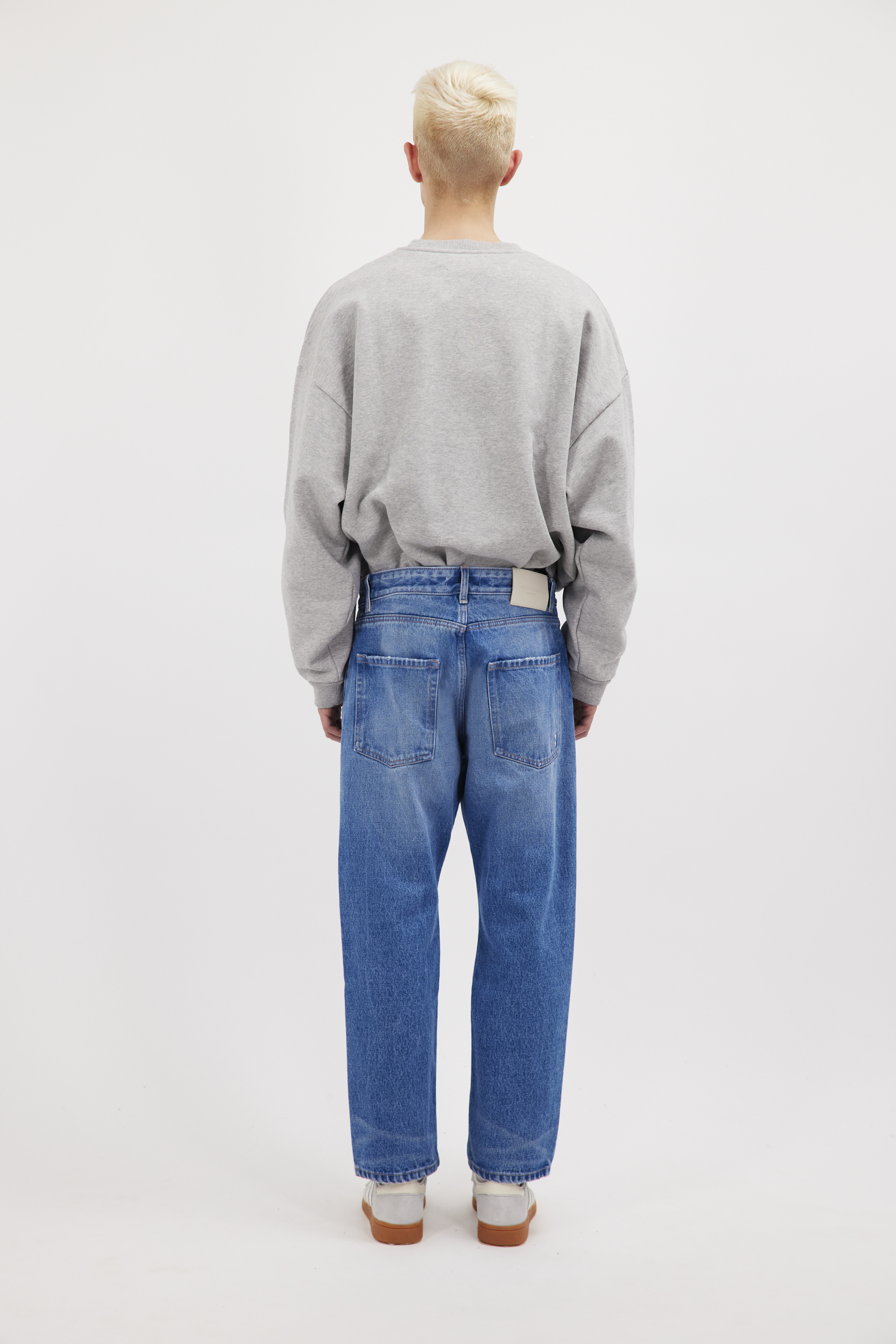 Back view of Josh Eco men’s carrot jeans in deep ocean wash, 100% rigid organic cotton denim, worn by a model with a gray sweatshirt.