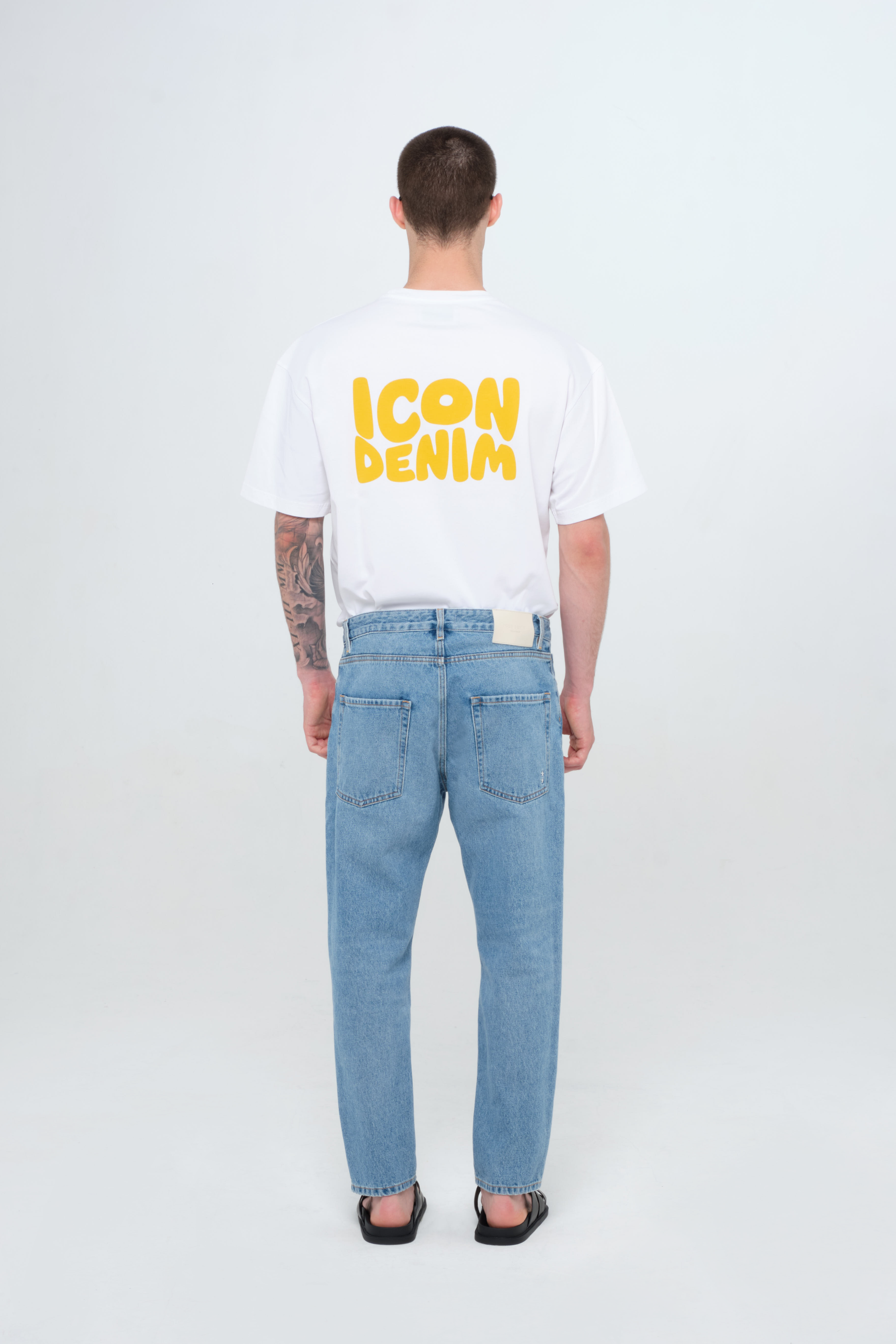 Back view of Josh Eco men’s carrot jeans in medium wash, 100% rigid organic cotton denim, worn by a model with a white t-shirt.
