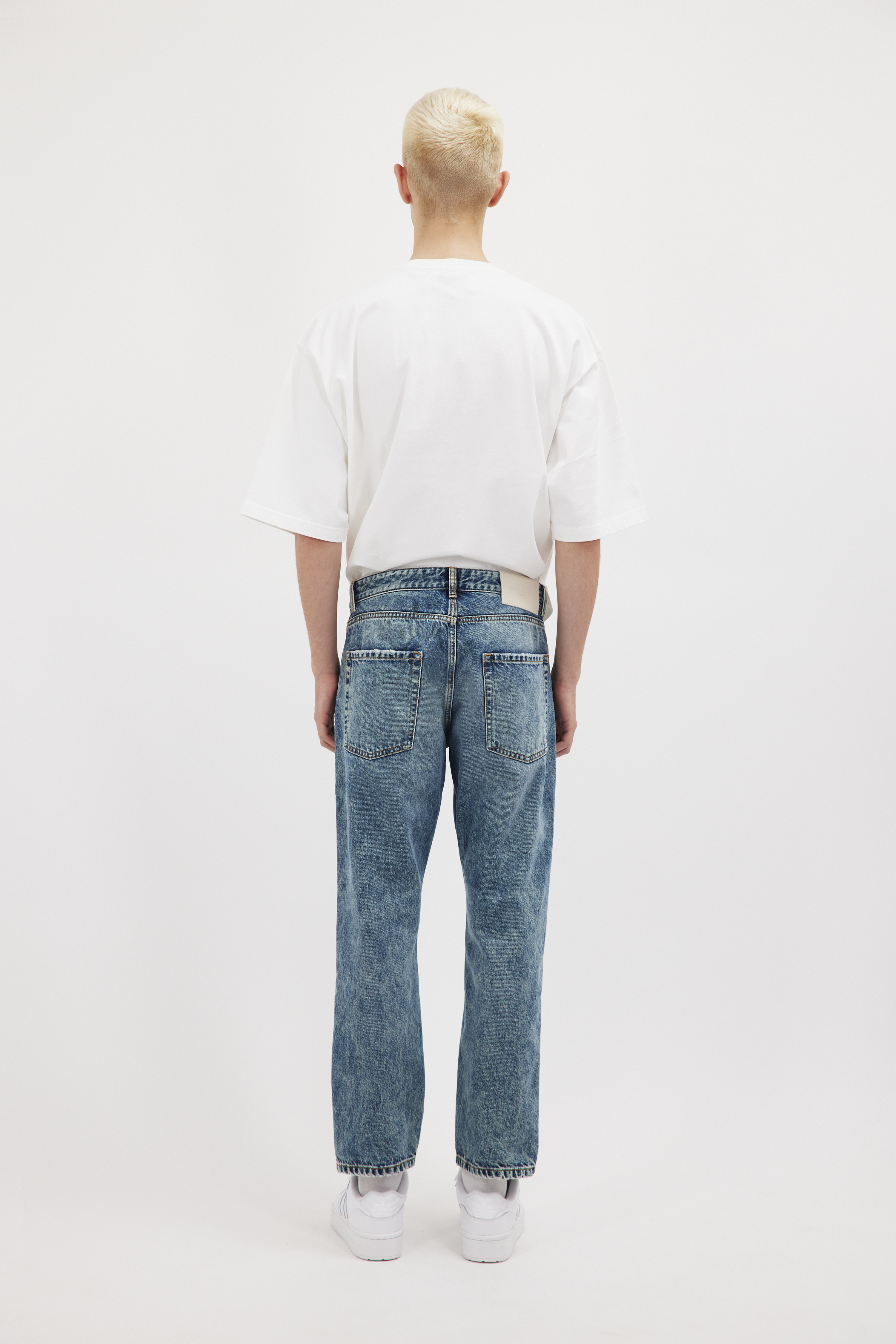 Back view of Josh men’s carrot jeans in aged stone wash, 100% rigid cotton denim, worn by a model with a white t-shirt.