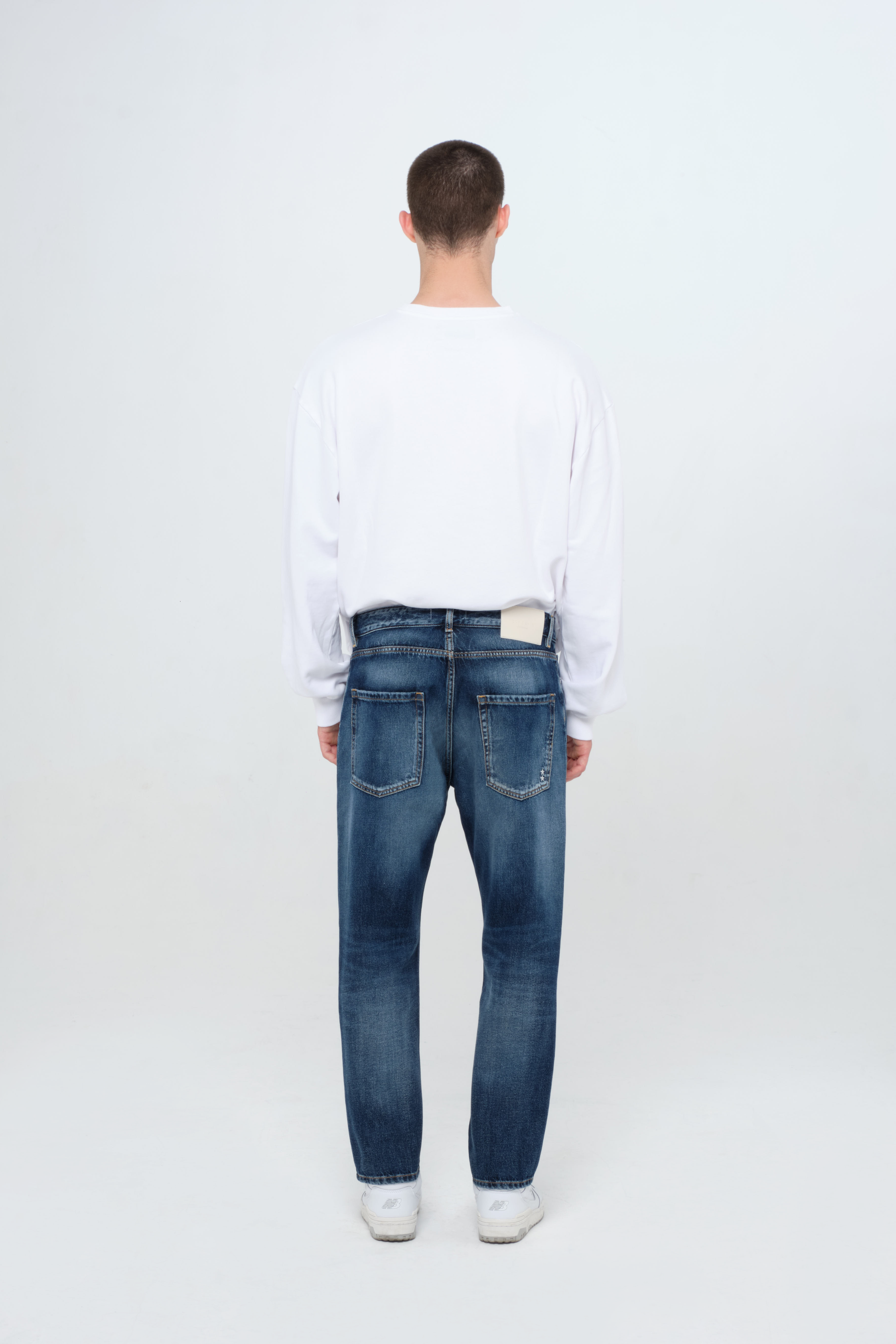 Back view of Josh men’s carrot jeans in dark wash, 100% rigid cotton denim, worn by a model with a white sweatshirt.
