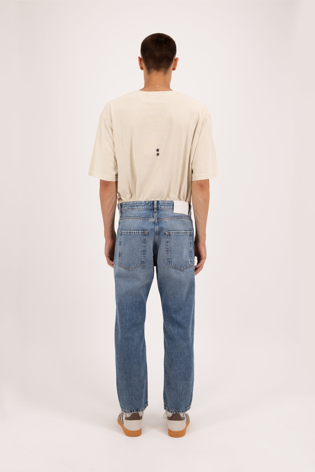Back view of Josh men’s carrot jeans in eclipse wash, 100% rigid cotton denim, worn by a model with a desert t-shirt.