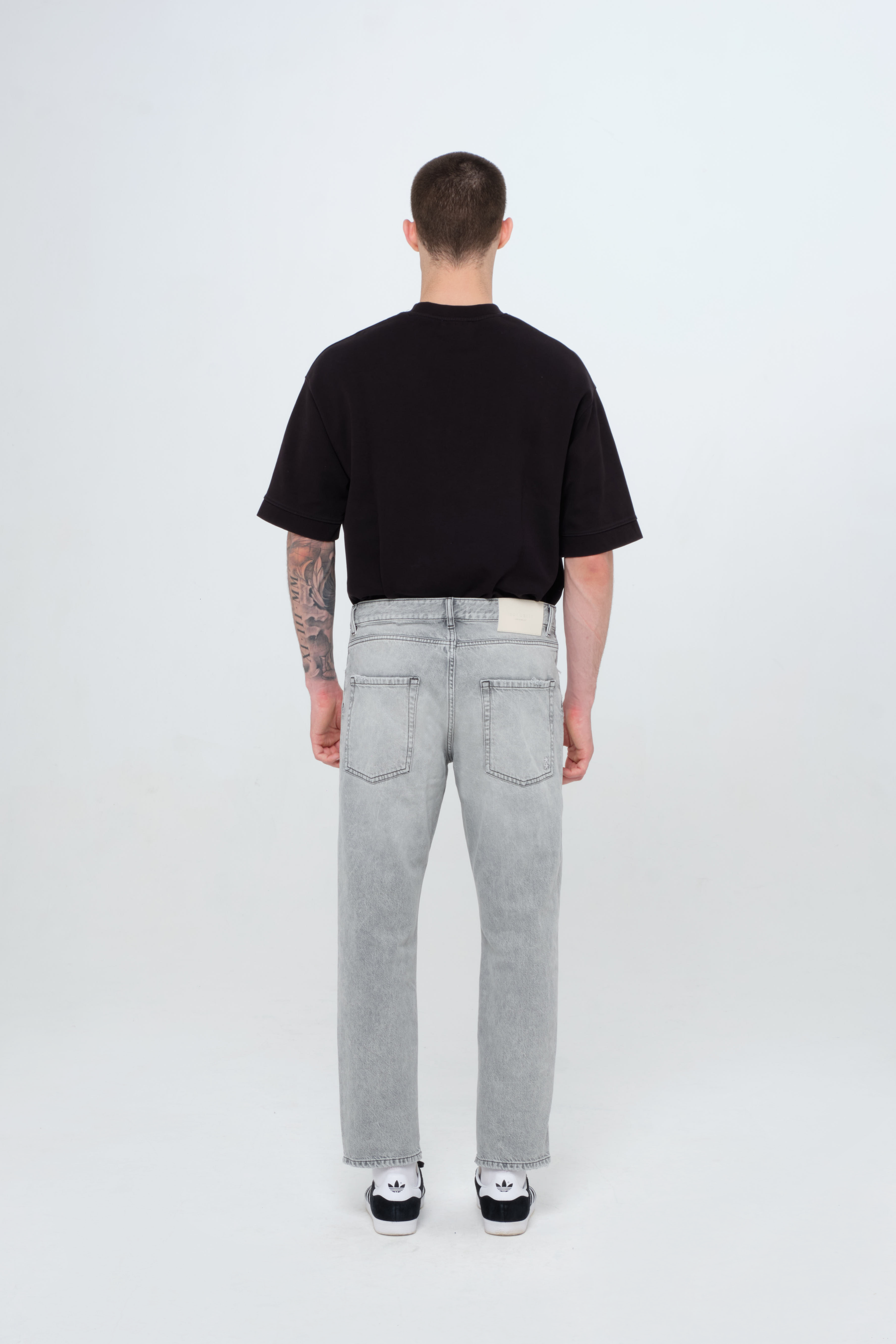 Back view of Josh men’s carrot jeans in gray wash, 100% rigid cotton denim, worn by a model with a black t-shirt.