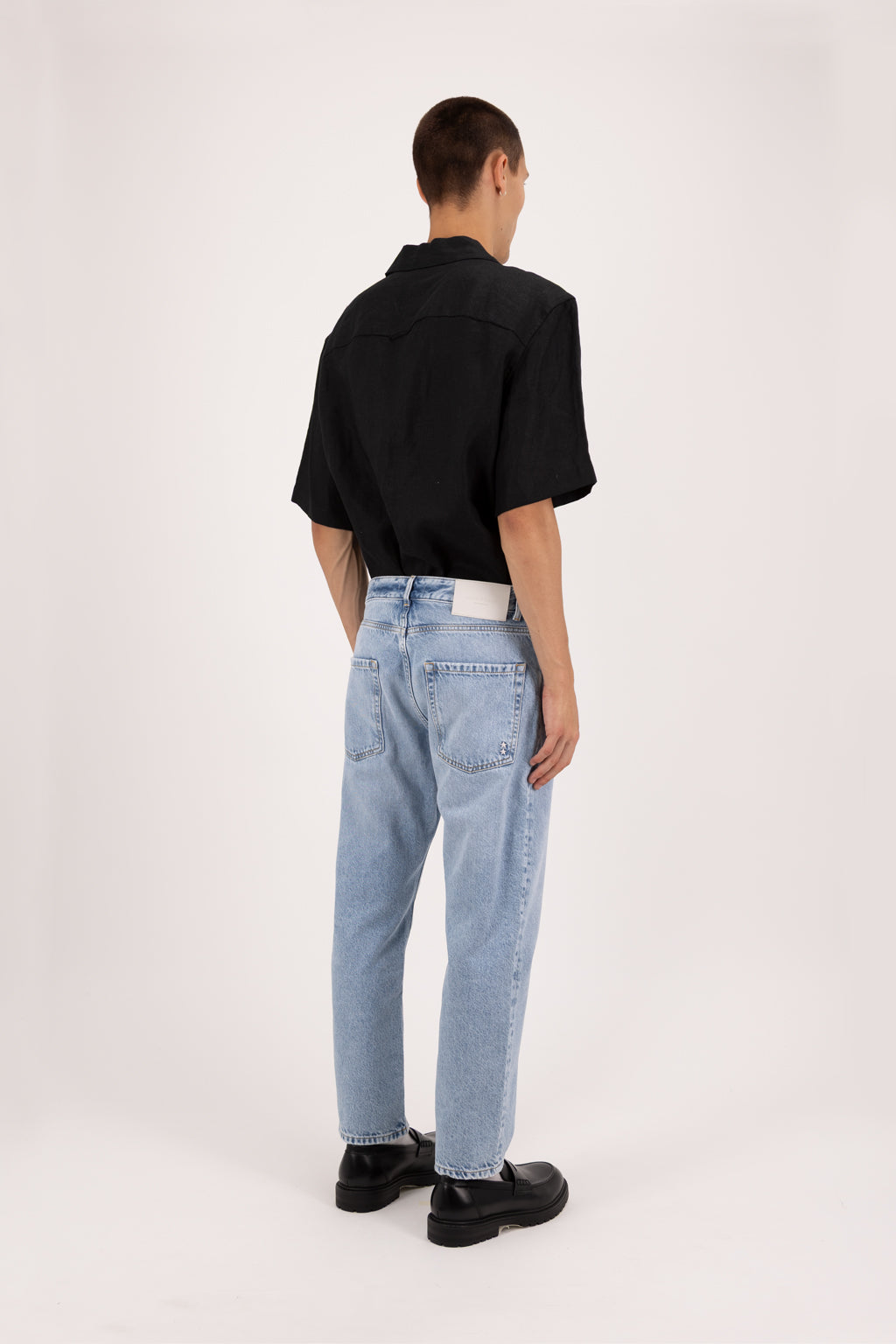 Back view of Josh men’s carrot jeans in sky blue wash, 100% rigid cotton denim, worn by a model with a black shirt.