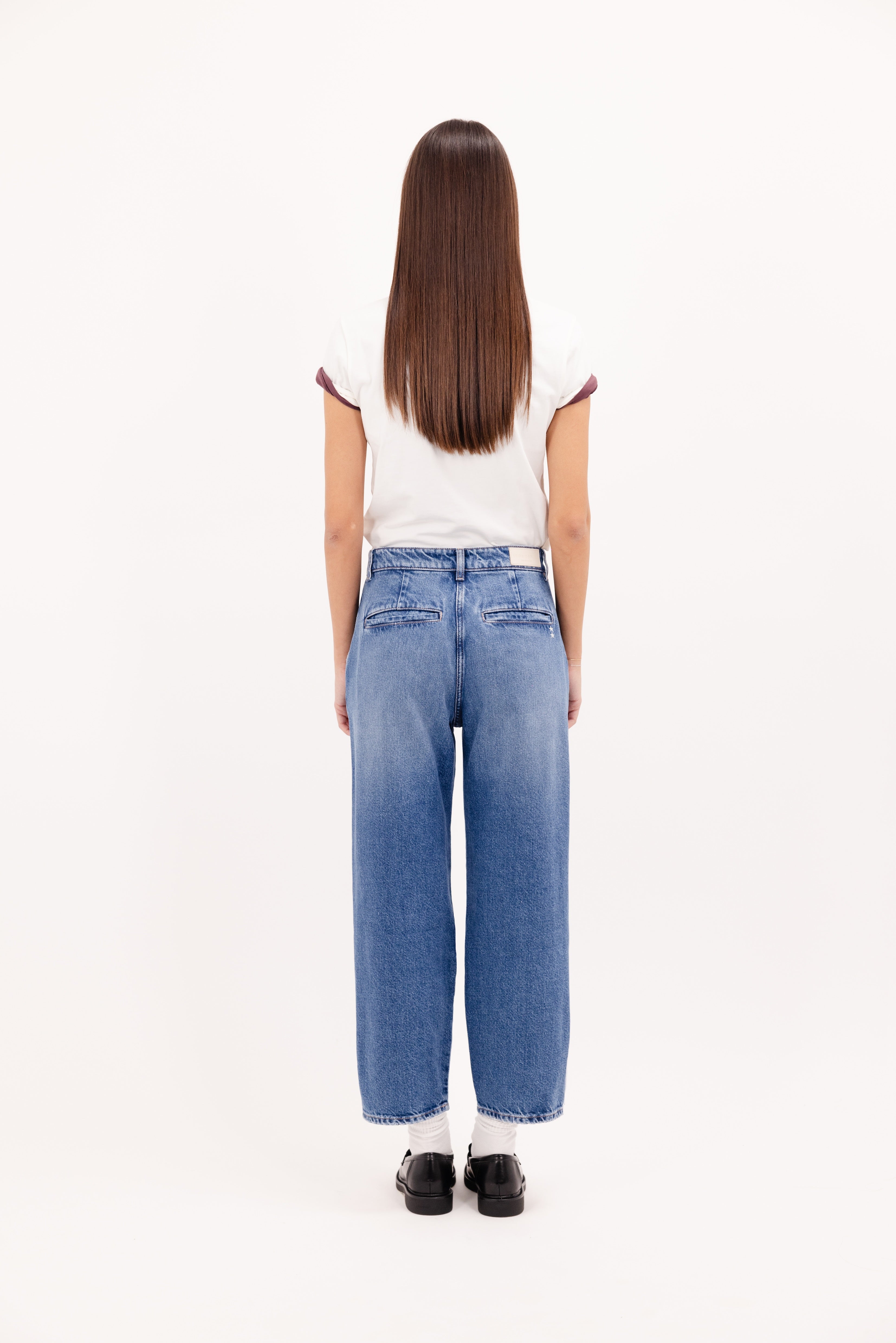 Back view of Juno women’s carrot jeans in eclipse wash, 100% rigid cotton denim, worn by a model with a white t-shirt.