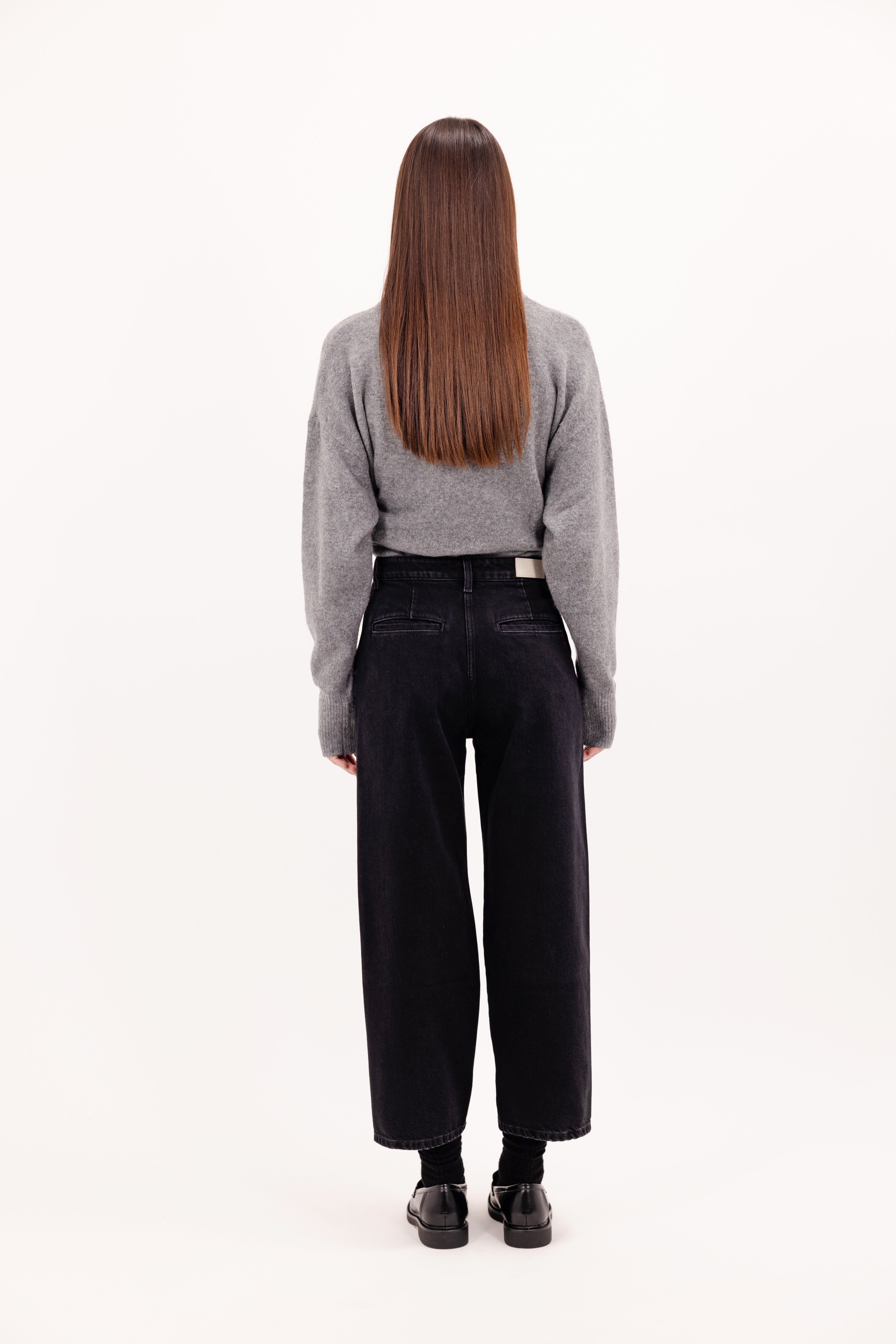 Back view of Juno women’s carrot jeans in graphite black wash, 100% rigid cotton denim, worn by a model with a gray knit.