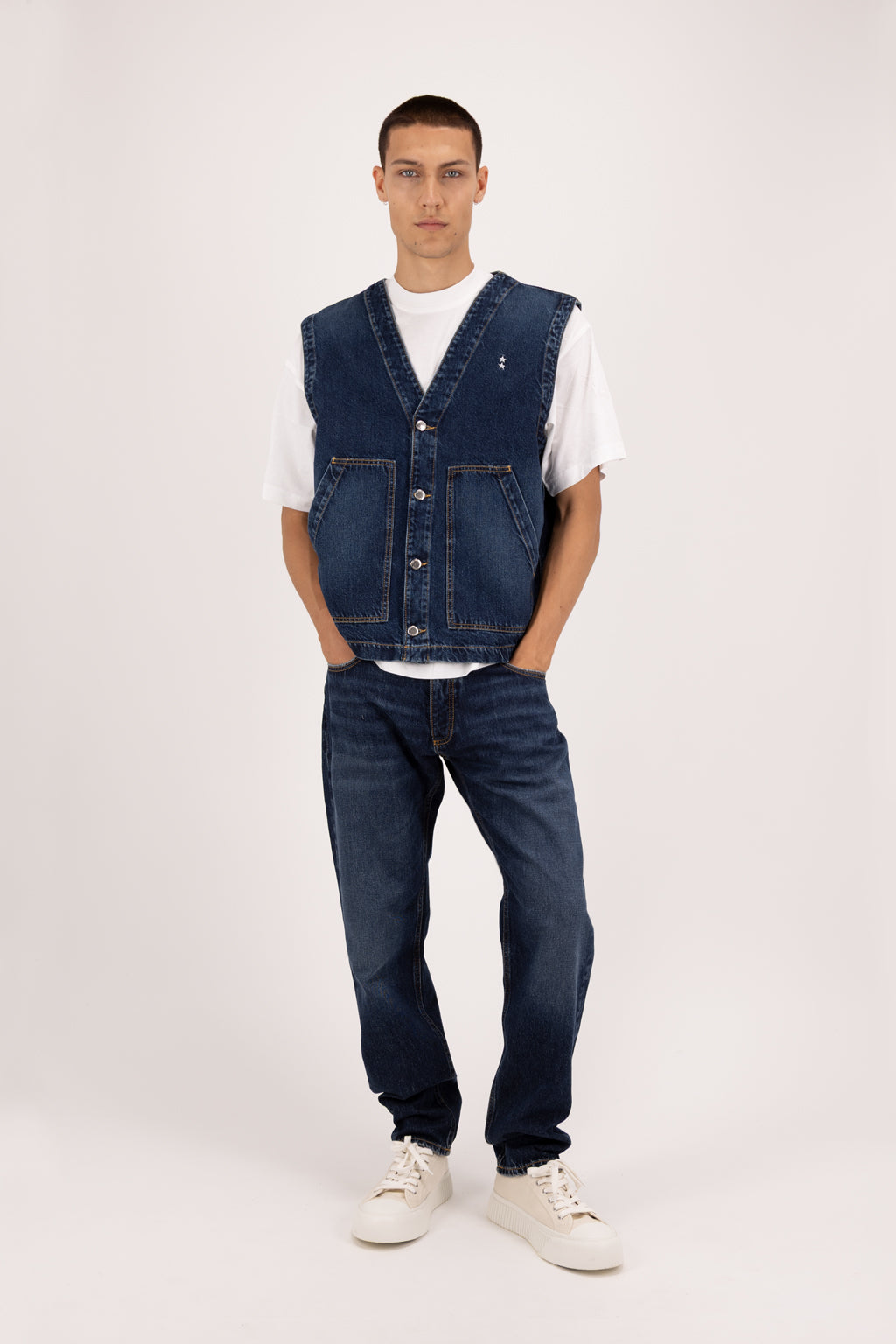Kanye men’s baggy jeans in deep blue wash, 100% rigid cotton denim, worn by a model with a denim vest.