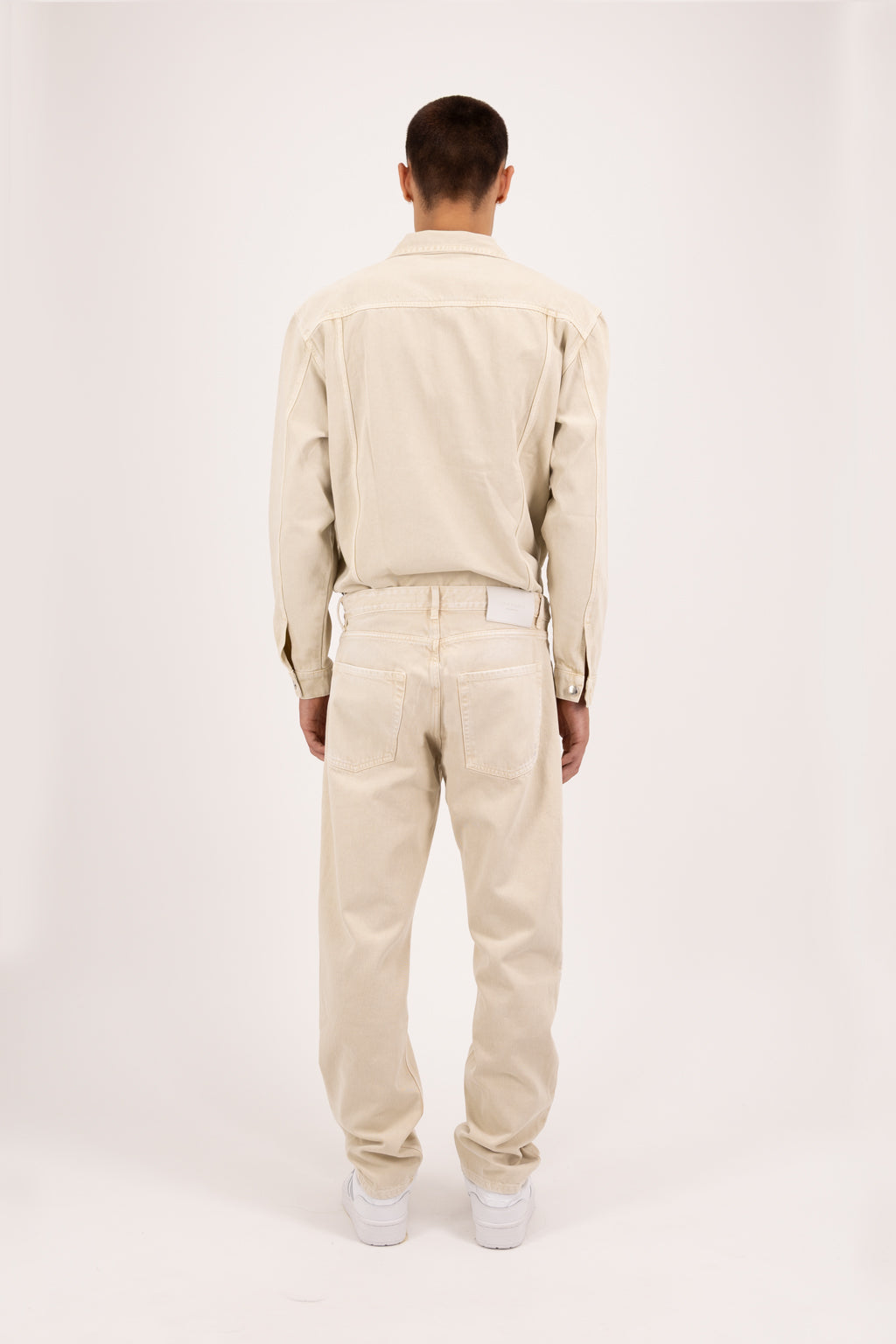 Back view of Kanye men’s baggy jeans in desert wash, 100% rigid soft cotton denim, worn by a model with a denim jacket.