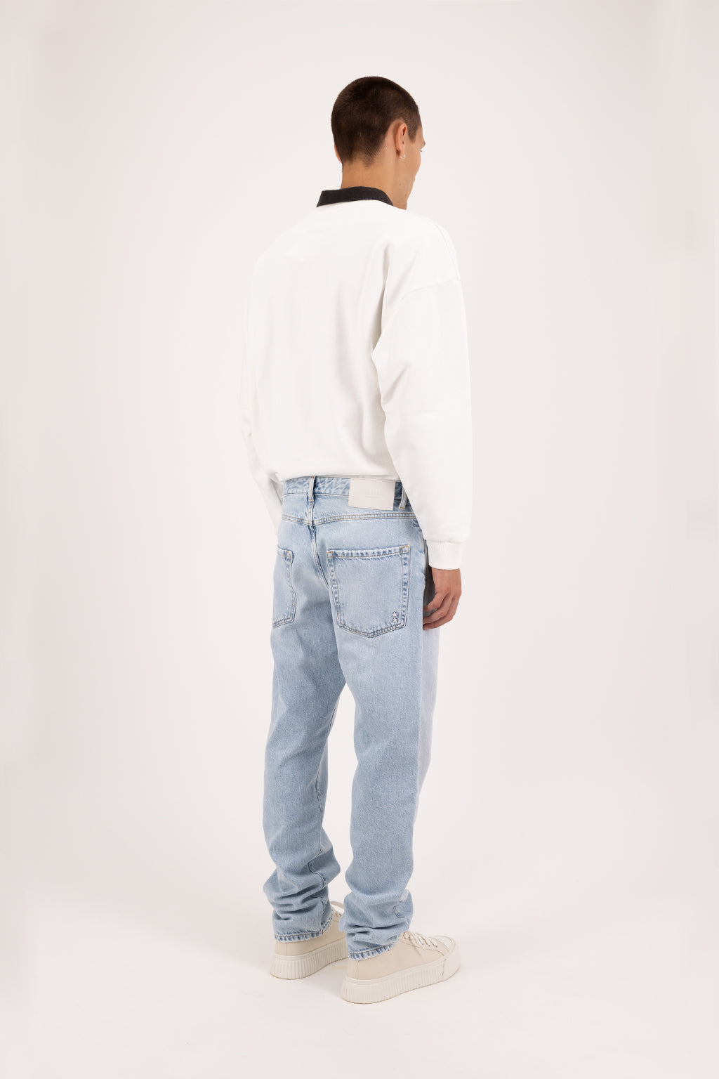 Back view of Kanye men’s baggy jeans in sky blue wash, 100% rigid cotton denim, worn by a model with a white sweatshirt.