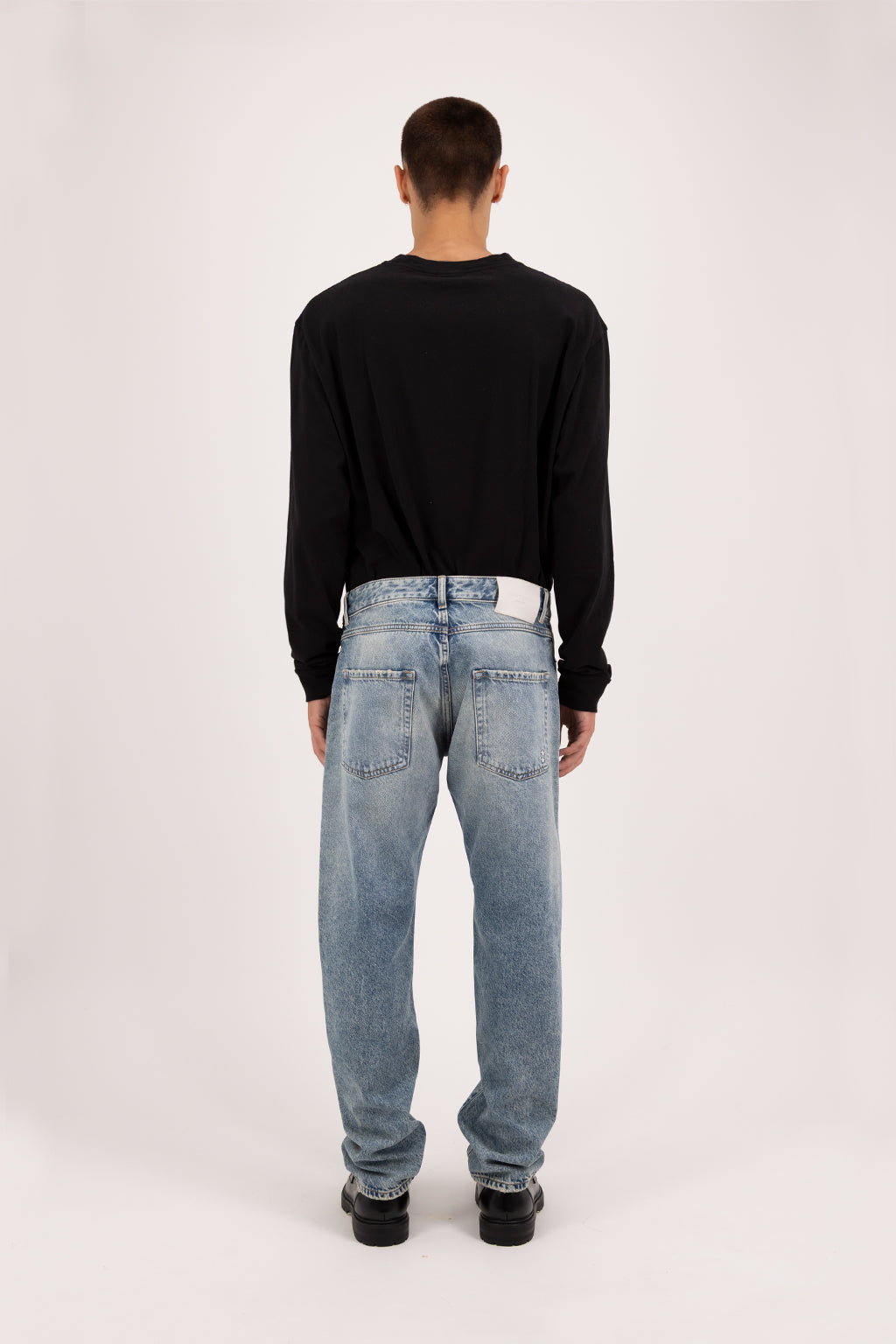 Back view of Kanye men’s baggy jeans in smoke blue wash, 100% rigid cotton denim, worn by a model with a black sweatshirt.