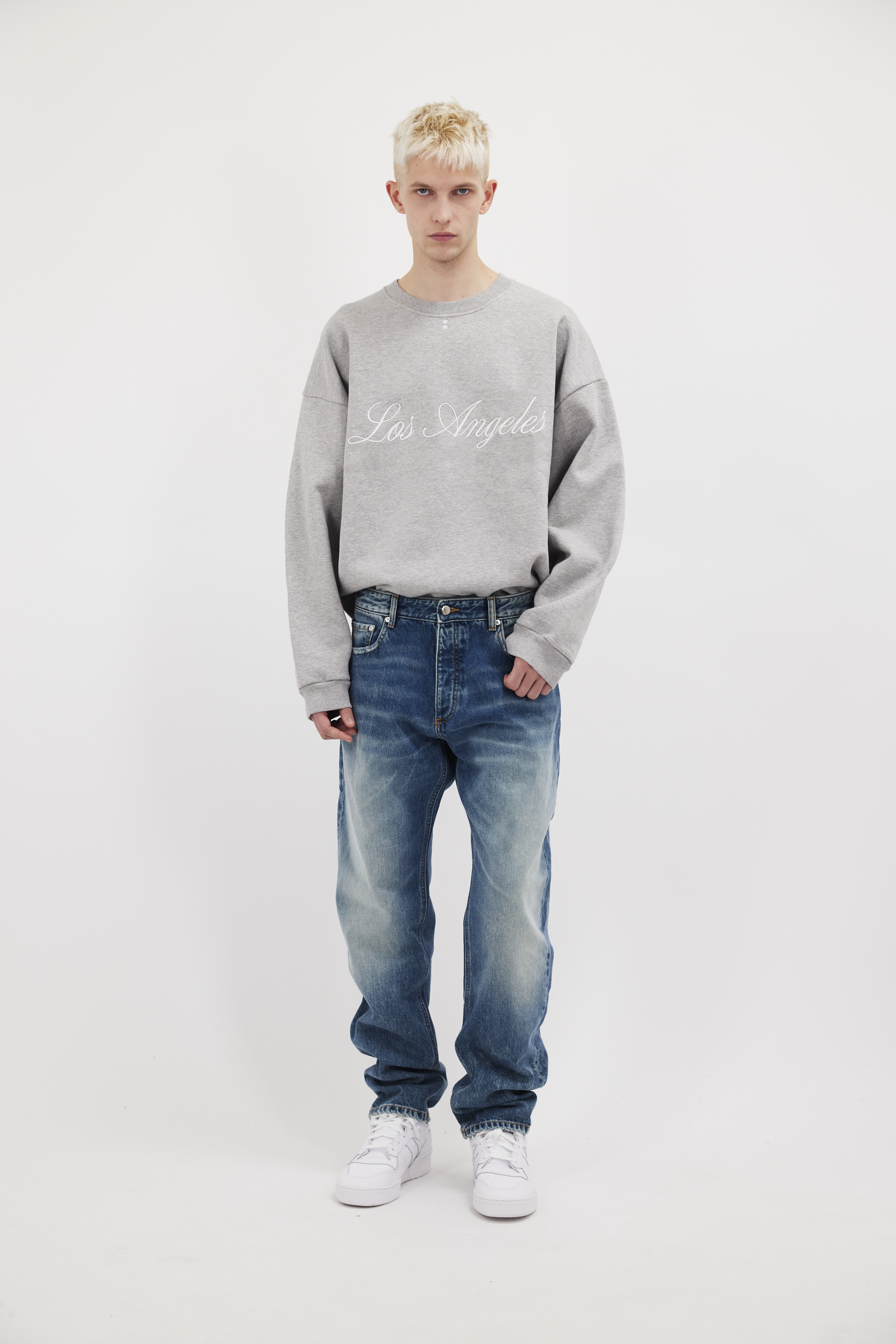 Kanye men’s loose jeans in aged stone wash, 100% rigid cotton denim, worn by a model with a gray sweatshirt.