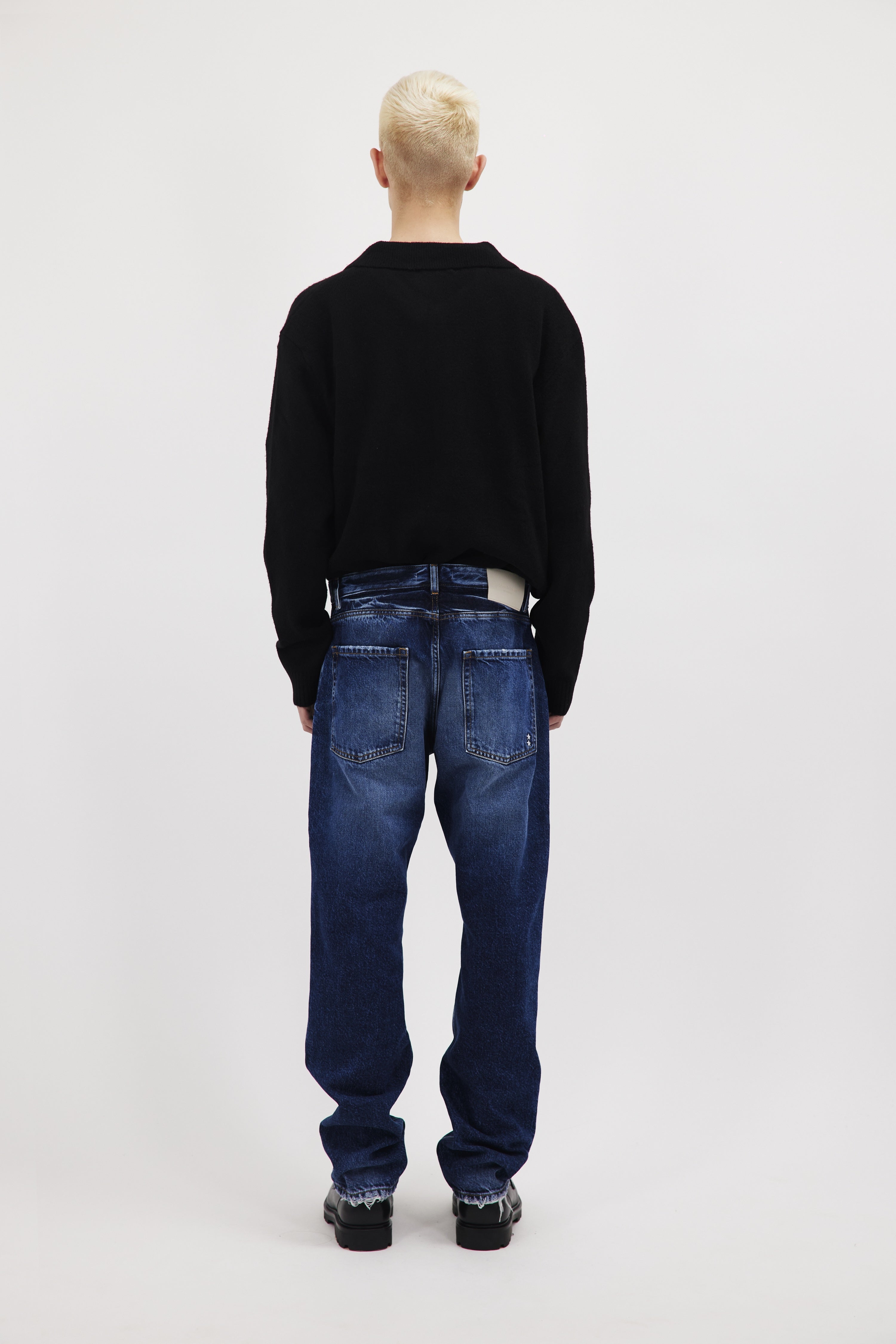 Back view of Kanye men’s loose jeans in eclipse wash, 100% rigid cotton denim, worn by a model with a black long sleeve.