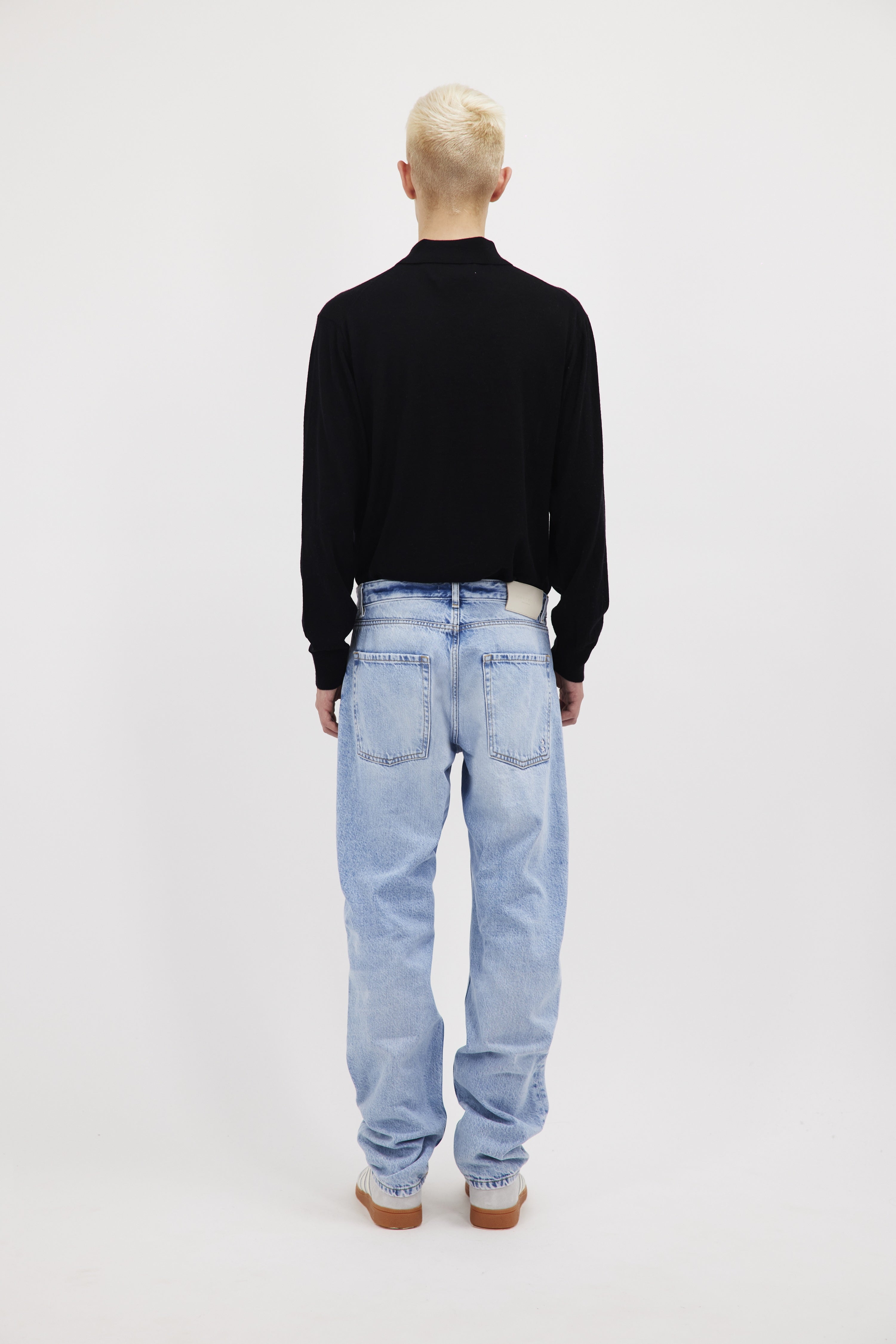 Back view of Kanye men’s loose jeans in sky blue wash, 100% rigid cotton denim, worn by a model with a black longsleeve.