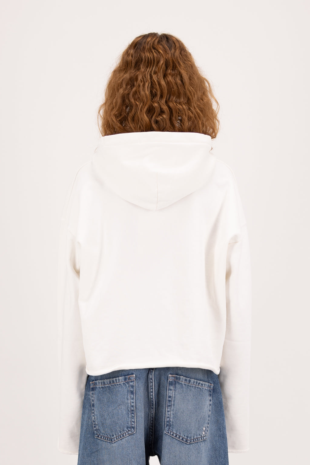 Back view of Kay women’s cropped hoodie in white, 100% cotton, worn by a model with jeans.