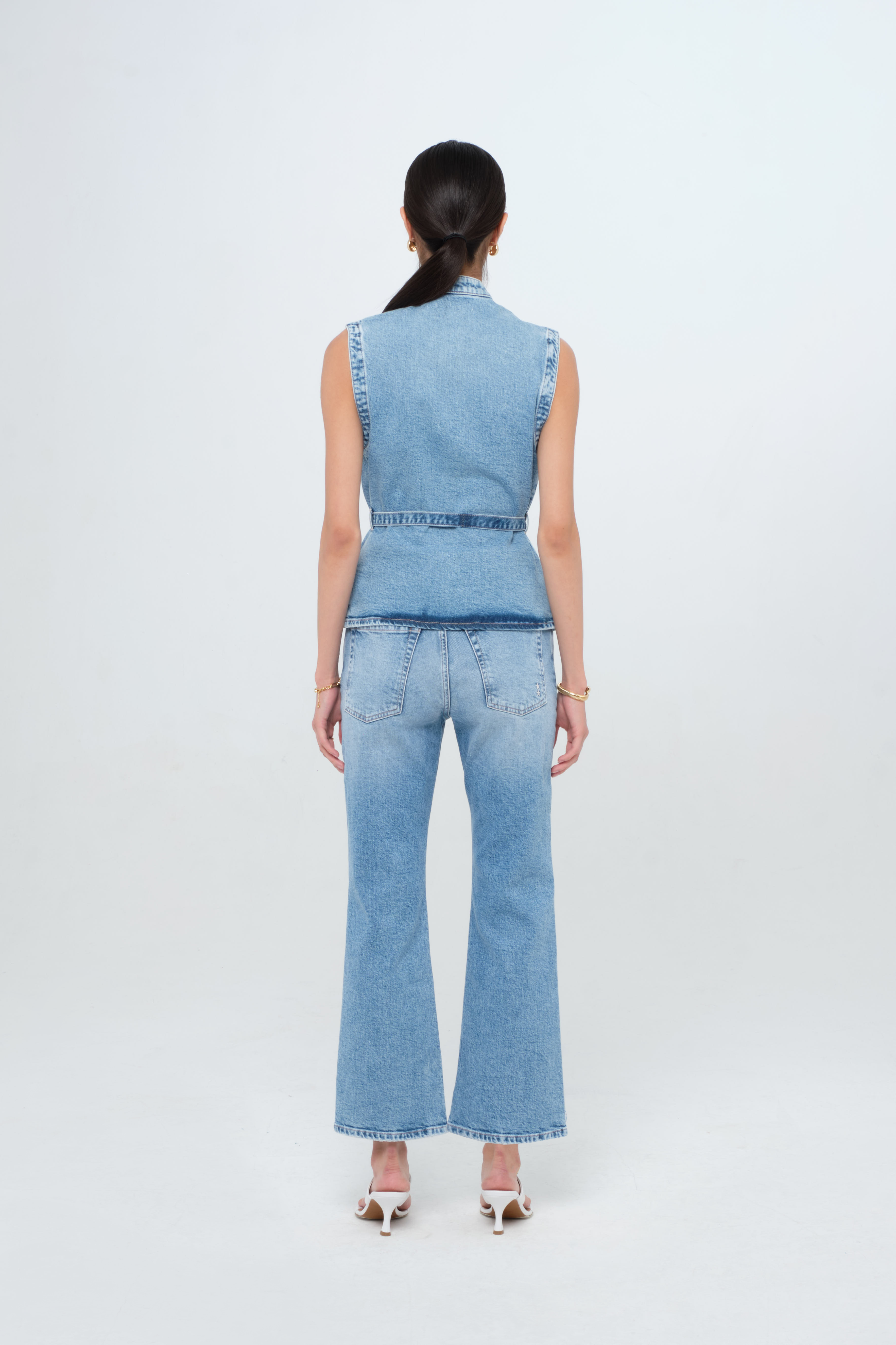 Back view of Kelly women’s vest in medium wash, 100% rigid cotton denim, worn by a model with jeans.