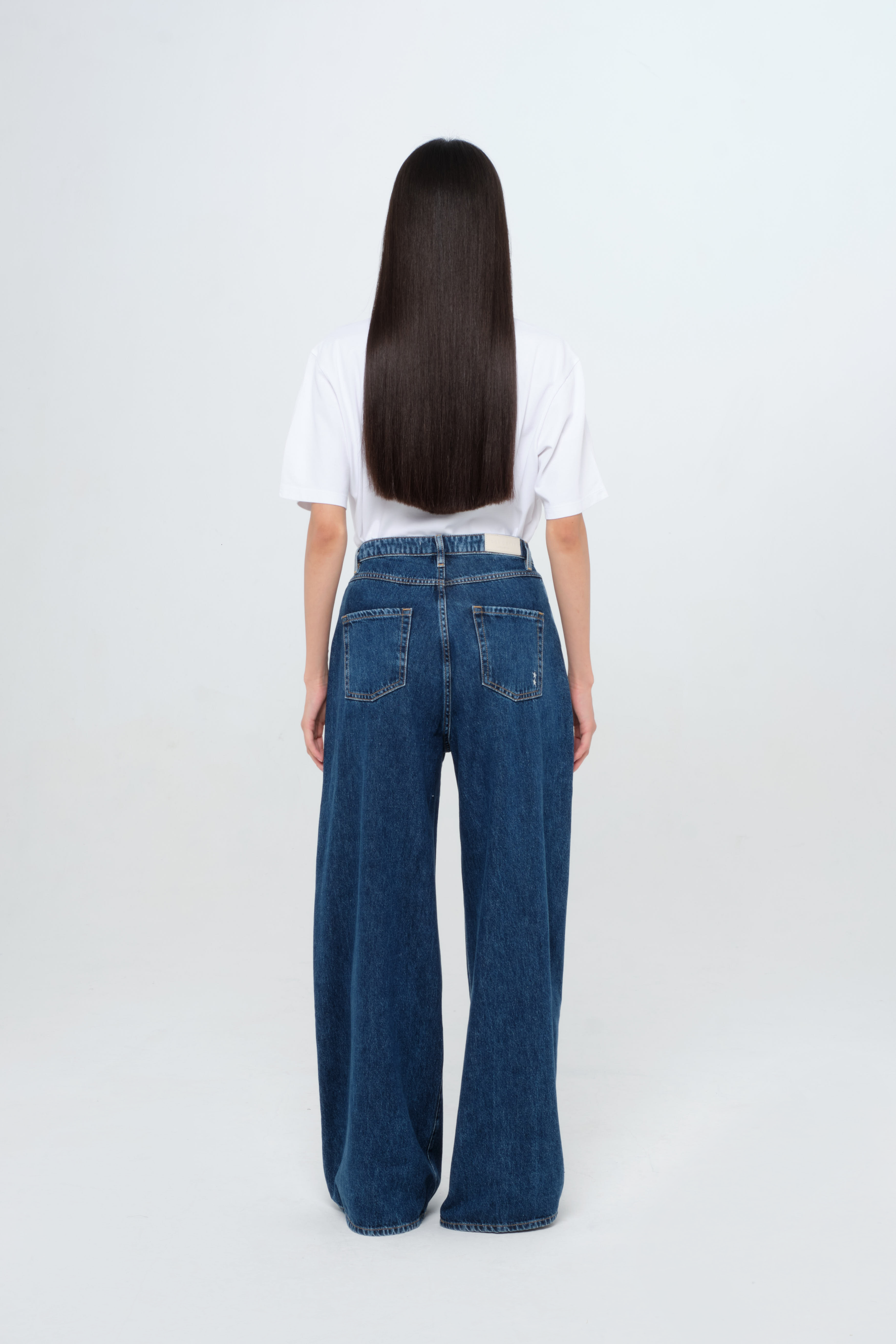 Back view of Kendall women’s wide leg jeans in dark wash, 100% rigid cotton denim, worn by a model with a white t-shirt.
