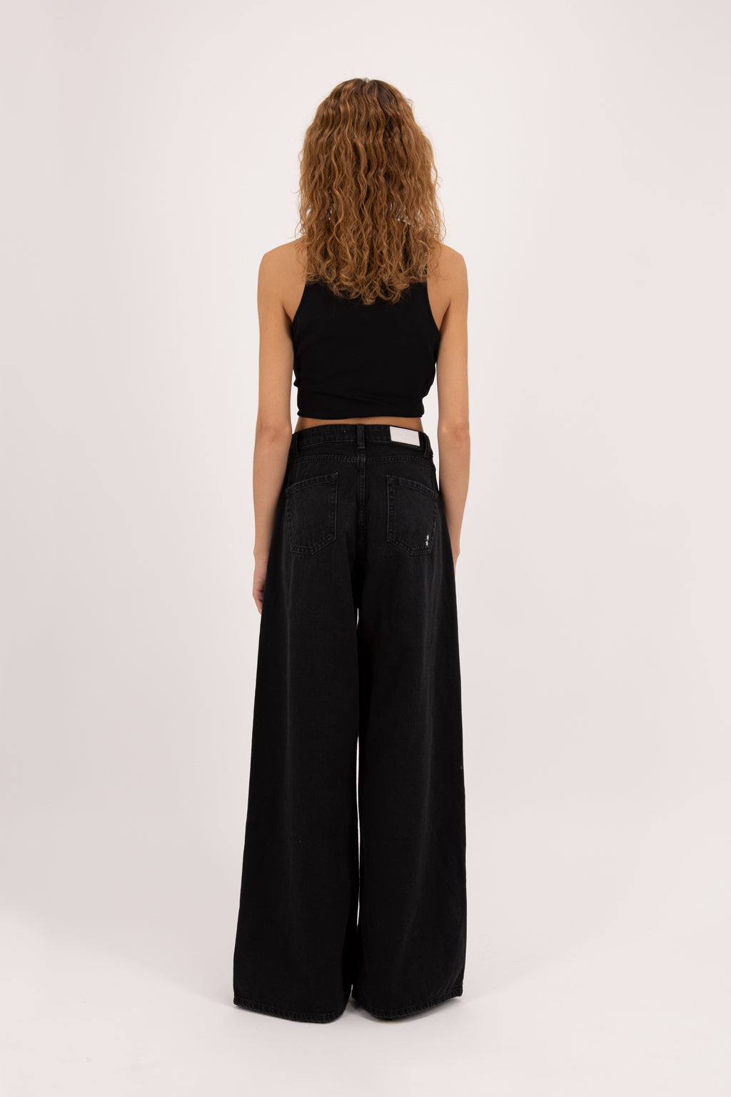 Back view of Kendall women’s wide leg jeans in graphite black wash, 100% rigid cotton denim, worn by a model with a black top.