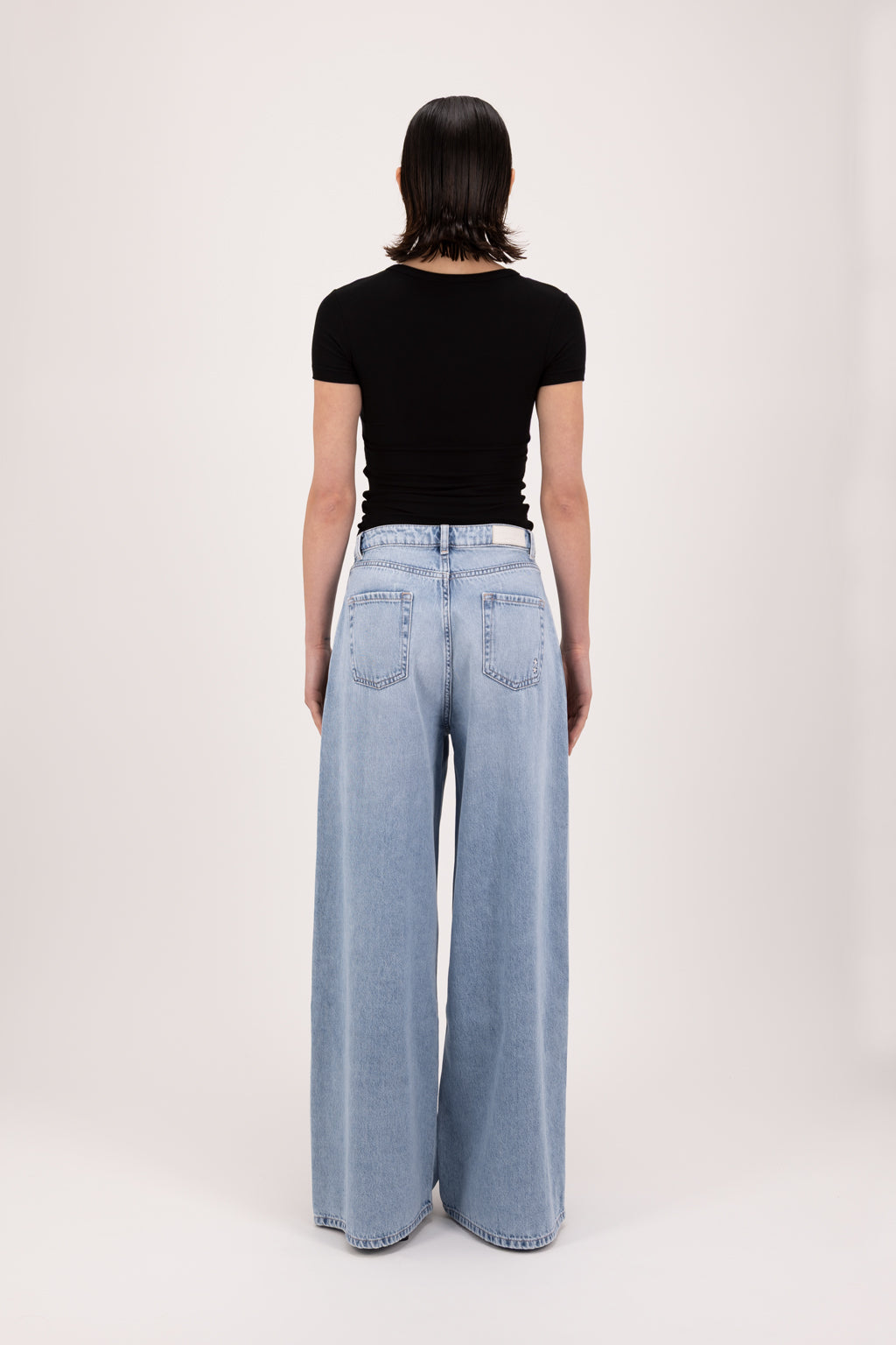 Back view of Kendall women’s wide leg jeans in sky blue wash, 100% rigid cotton denim, worn by a model with a black top.