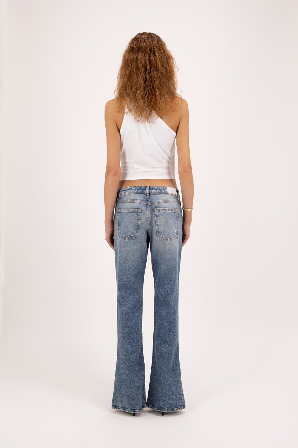 Back view of Kendy women’s slim flared leg jeans in smoke blue wash, 100% rigid cotton denim, worn by a model with a white top.