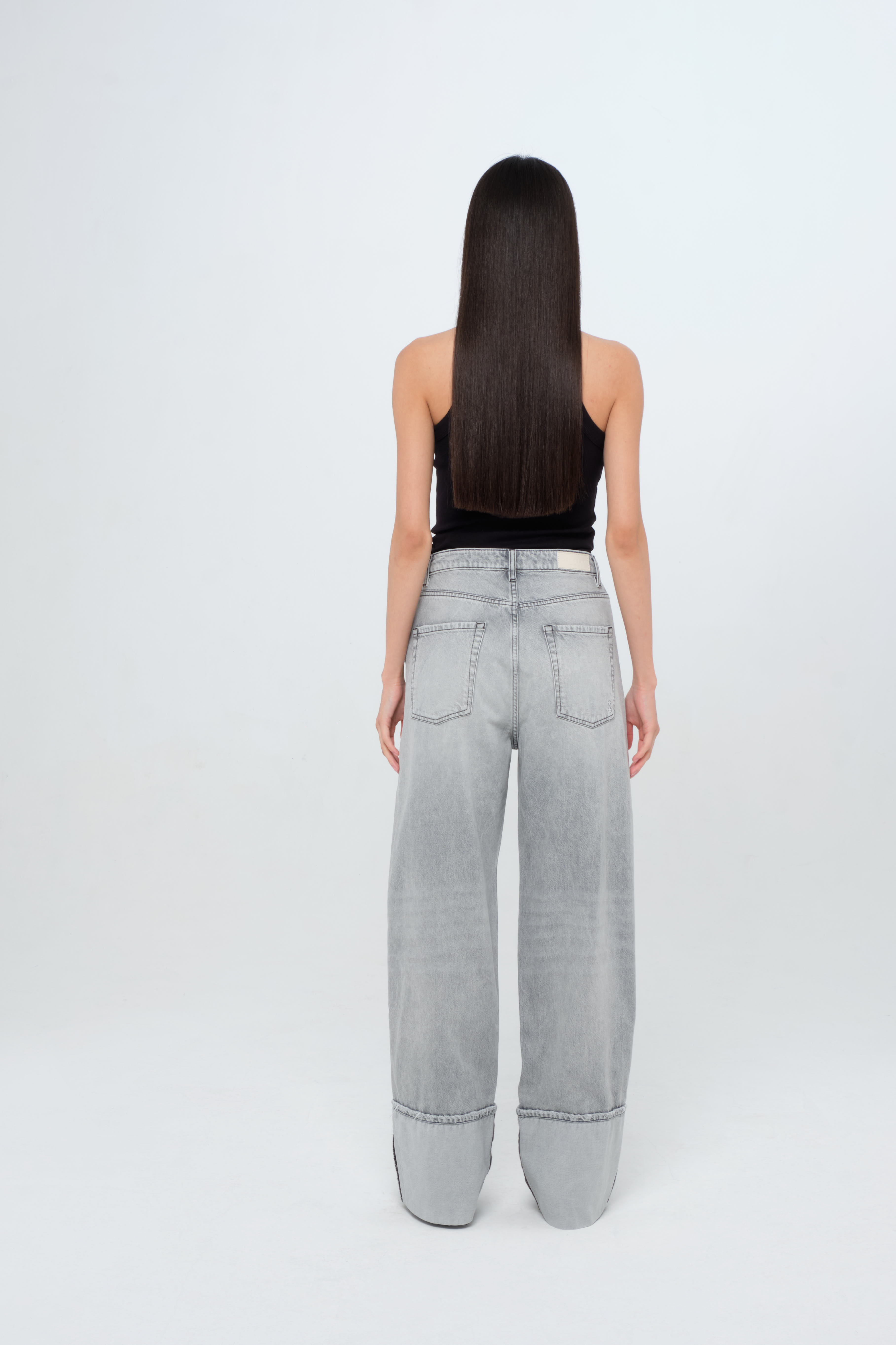 Back view of Kiki women’s wide leg jeans in gray wash, 100% rigid cotton denim, worn by a model with a black top.