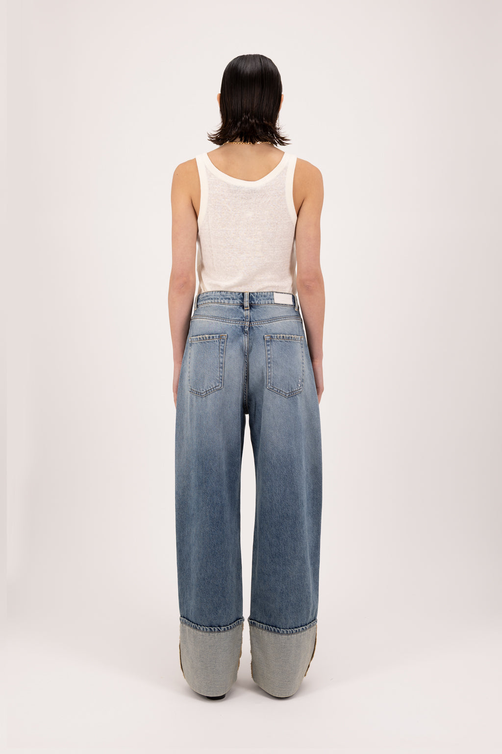 Back view of Kiki women’s wide leg jeans in smoke blue wash, 100% rigid cotton denim, worn by a model with a white tank top.
