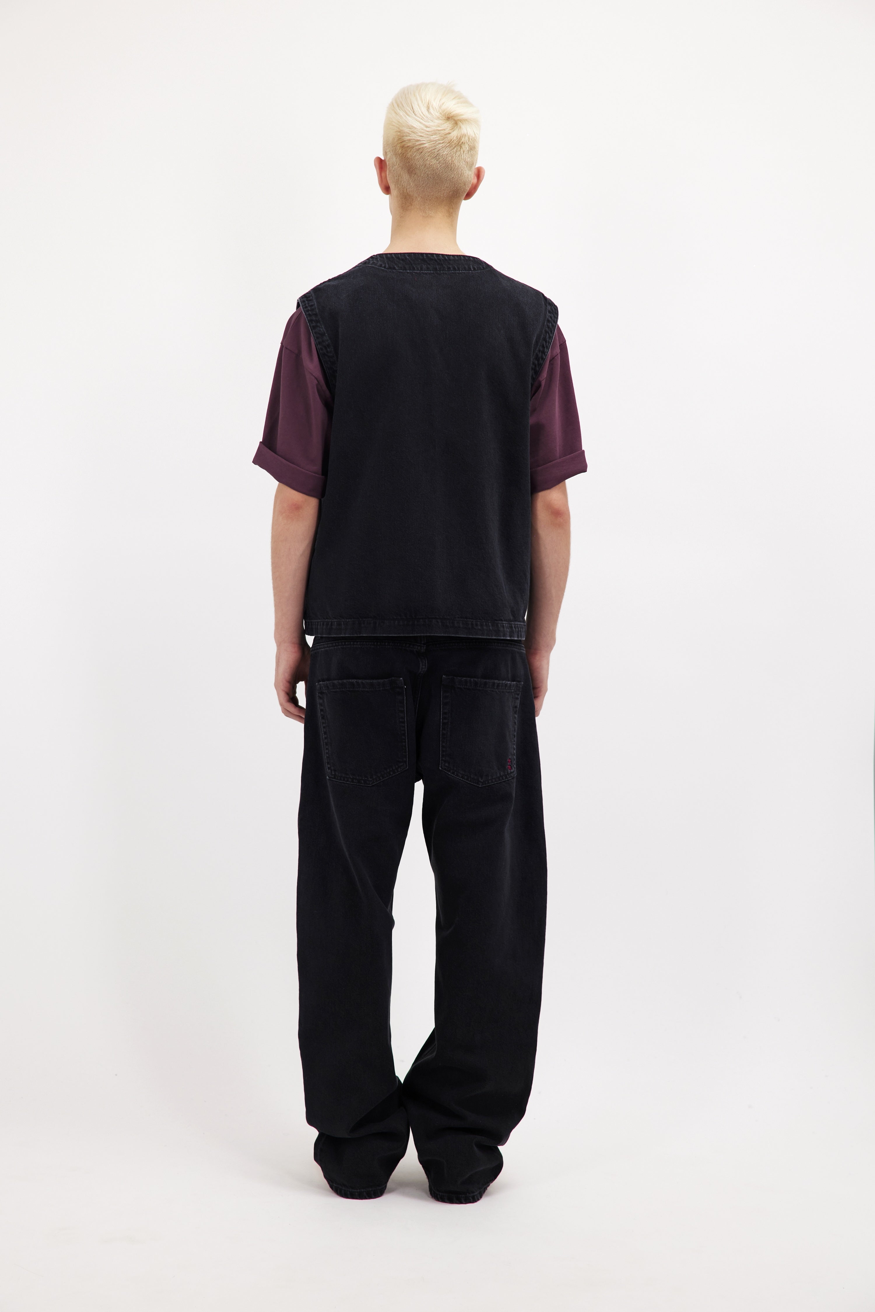 Back view of Kit men’s vest in graphite black wash, 100% rigid cotton denim, worn by a model with a cherry t-shirt.