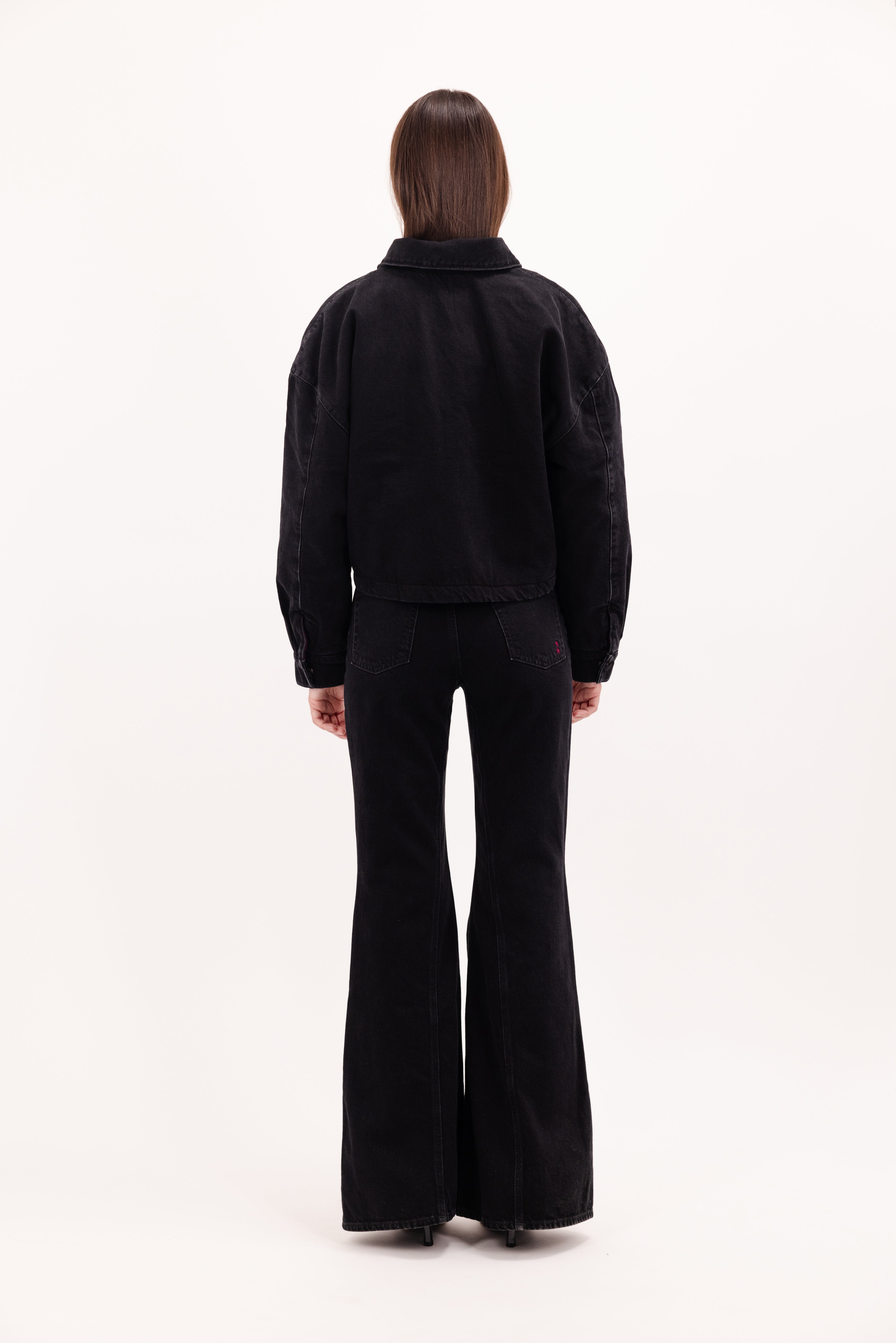 Back view of Kleo women’s jacket in graphite black wash, 100% rigid cotton denim, worn by a model with jeans.