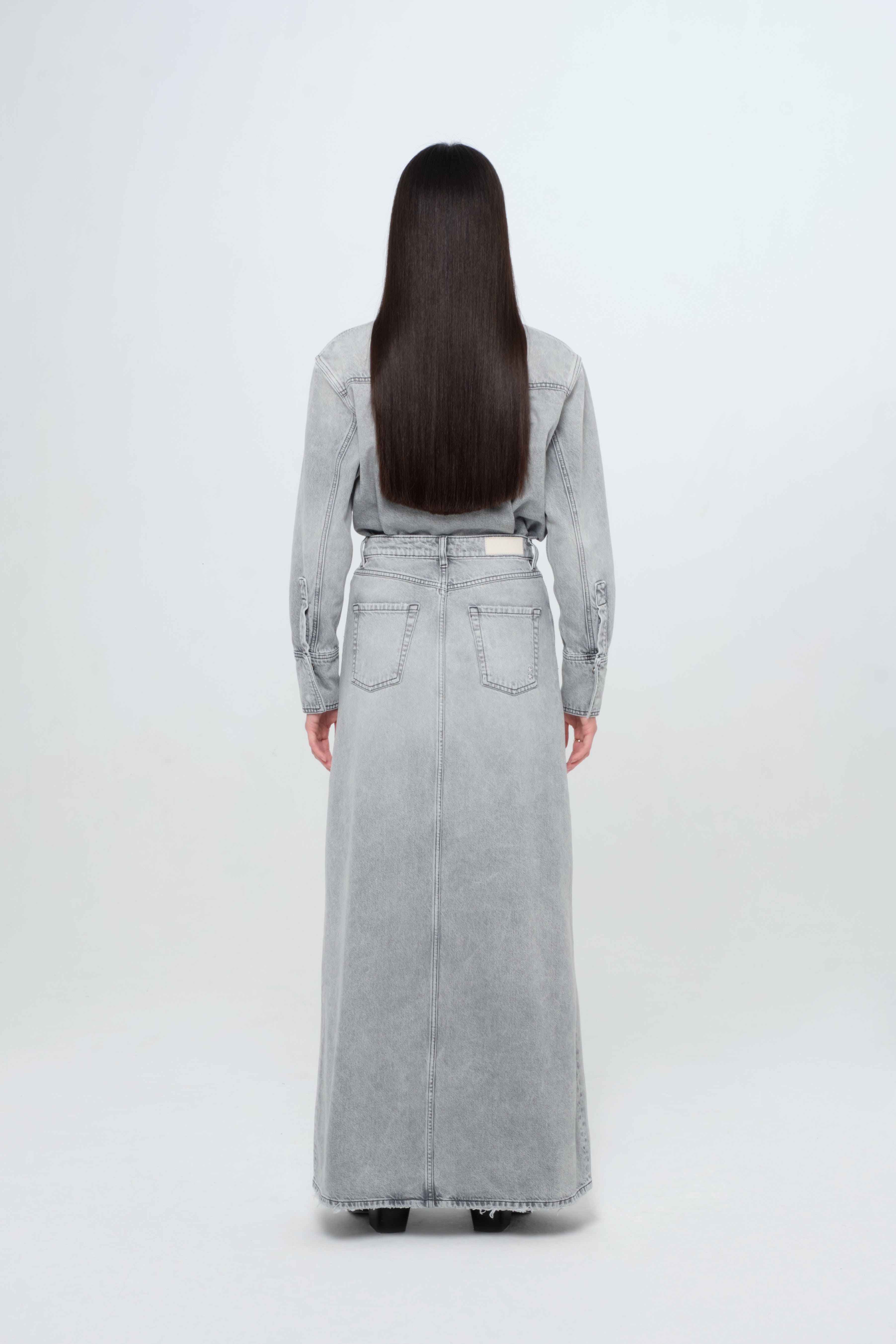 Back view of Lara women’s long skirt in gray wash, 100% rigid cotton denim, worn by a model with a gray wash denim shirt.