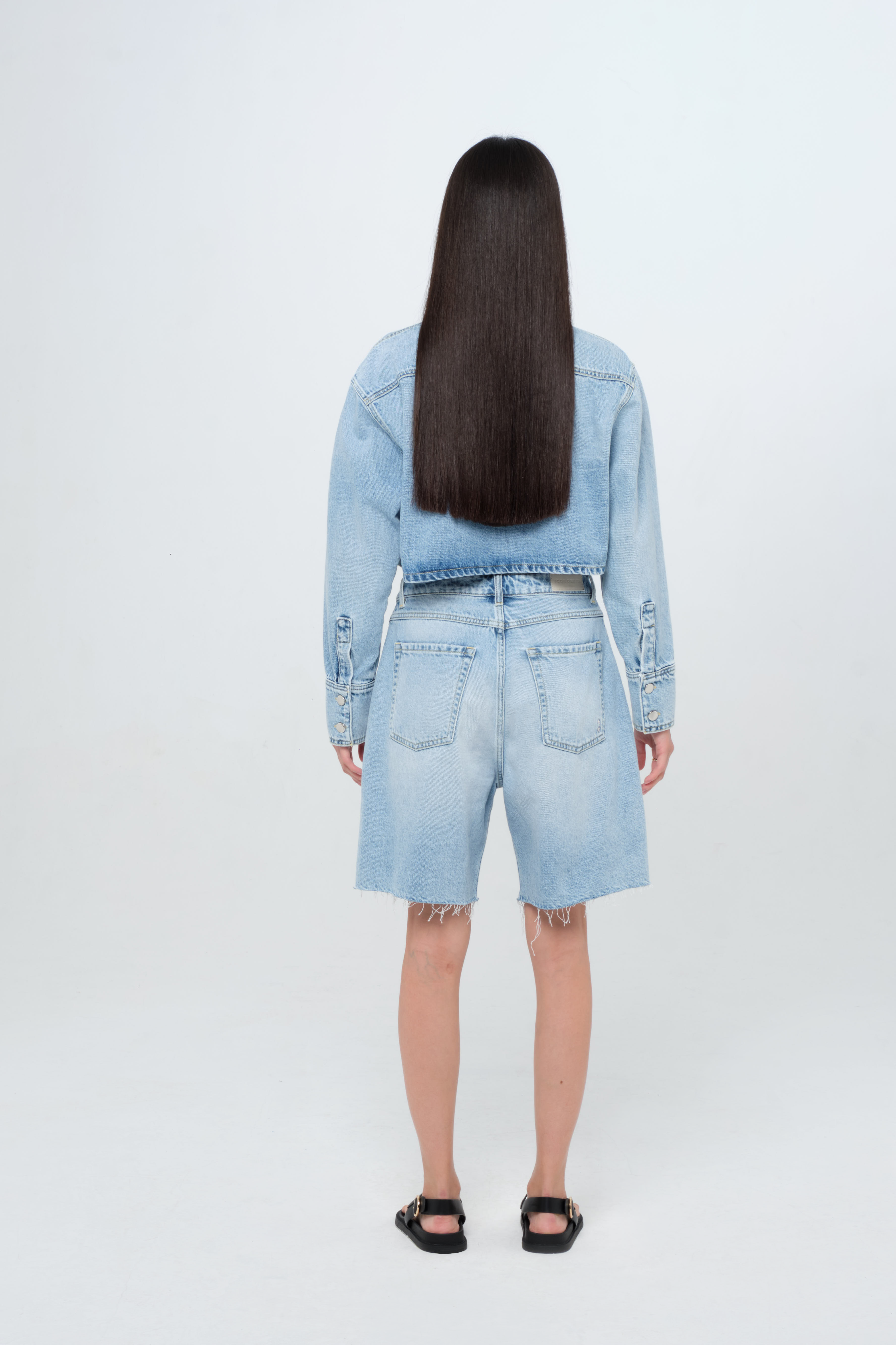 Back view of Lea women’s wide leg short jeans in light wash, 100% rigid cotton denim, worn by a model with a crop denim shirt.