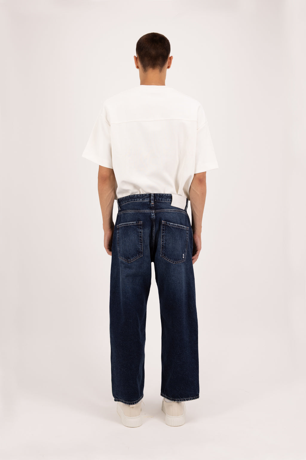 Back view of Leo men’s wide curt cropped jeans in deep blue wash, 100% rigid cotton denim, worn by a model with a white t-shirt.