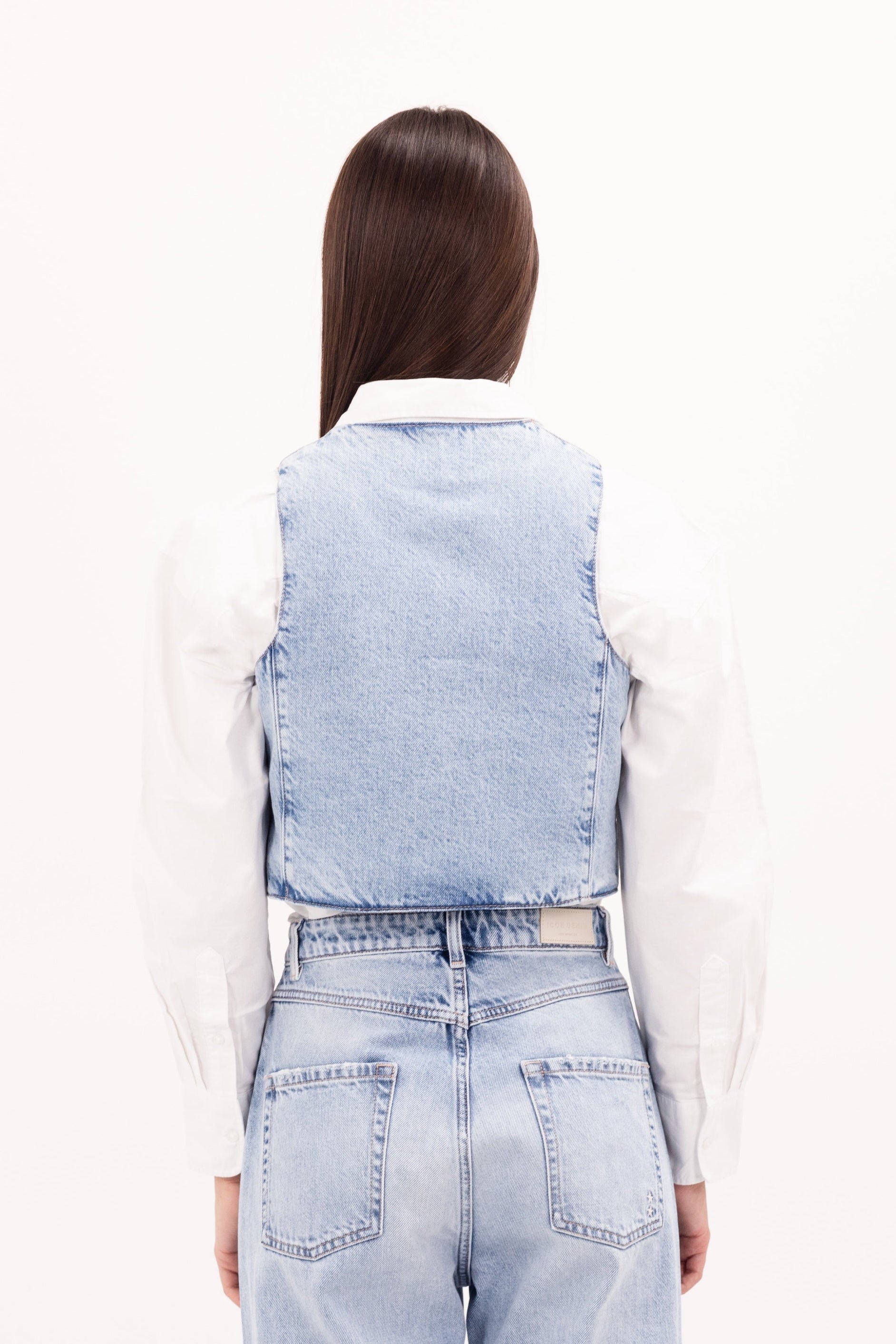 Back view of Liv women’s vest in sky blue wash, 100% rigid cotton denim, worn by a model with jeans.