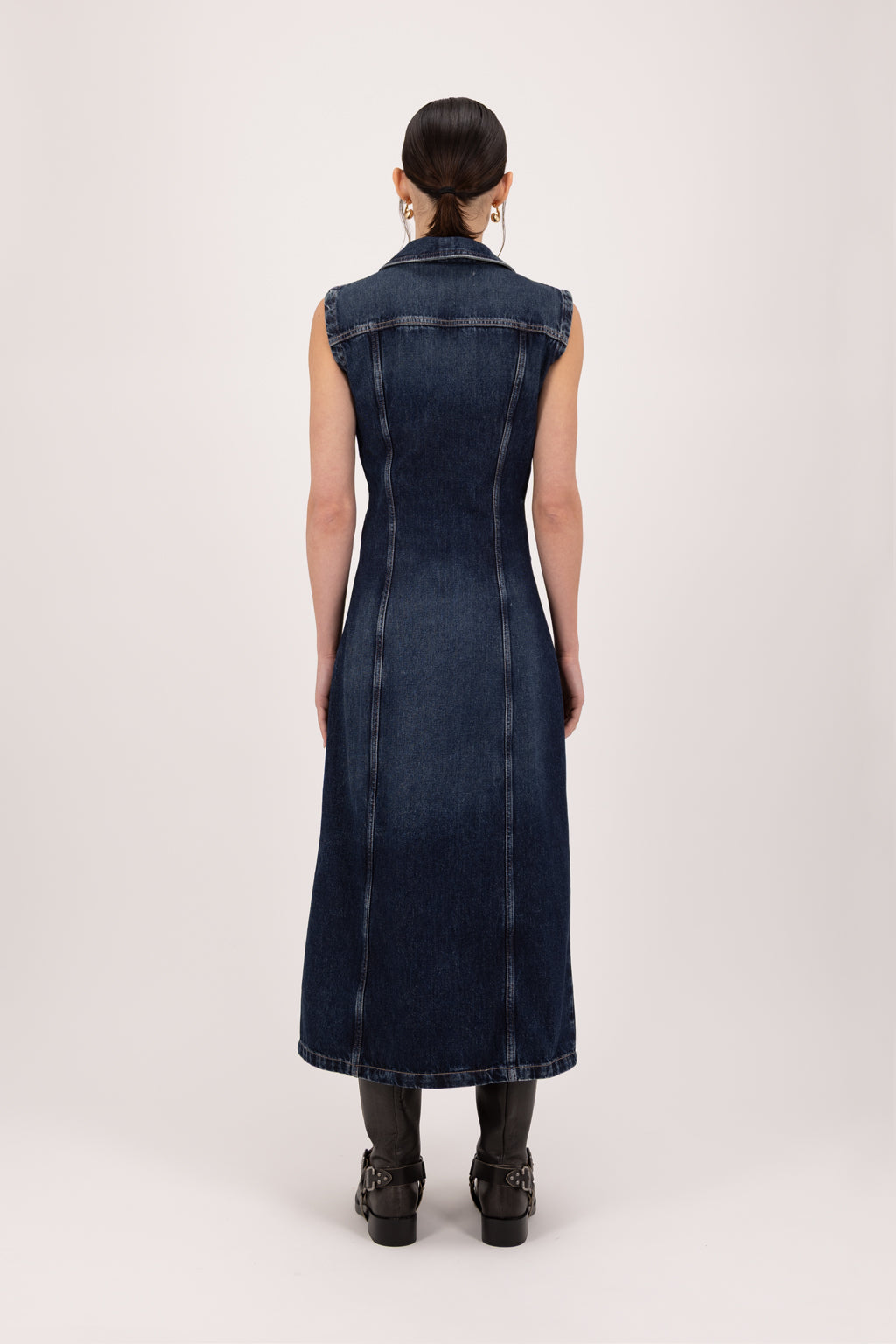 Back view of Ludy women’s dress in deep blue wash, 100% rigid soft cotton denim, worn by a model with shorts.