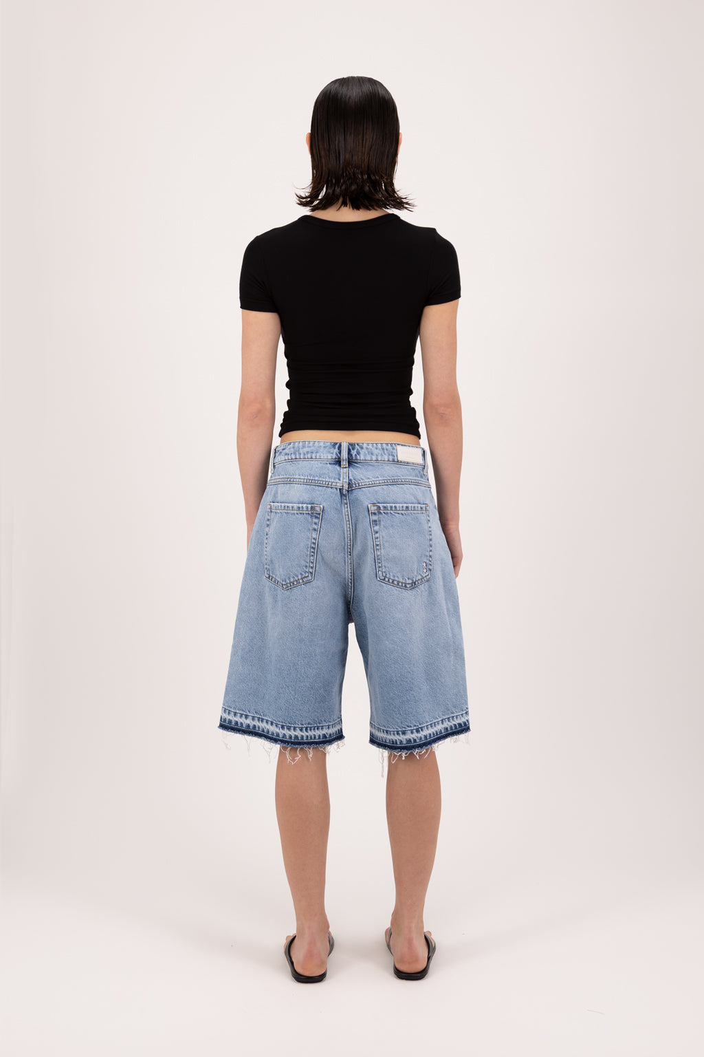 Back view of Lulu women’s wide leg short in sky blue wash, 100% rigid cotton denim, worn by a model with a black top.