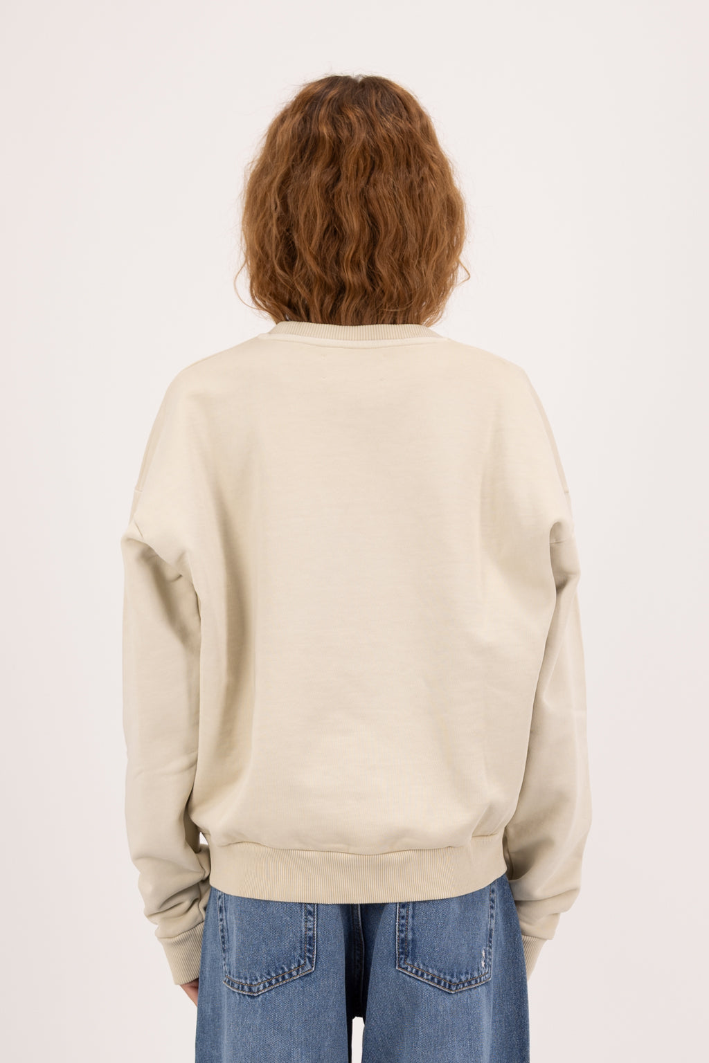 Back view of Mellie women’s sweatshirt in desert, 100% cotton, worn by a model with jeans.